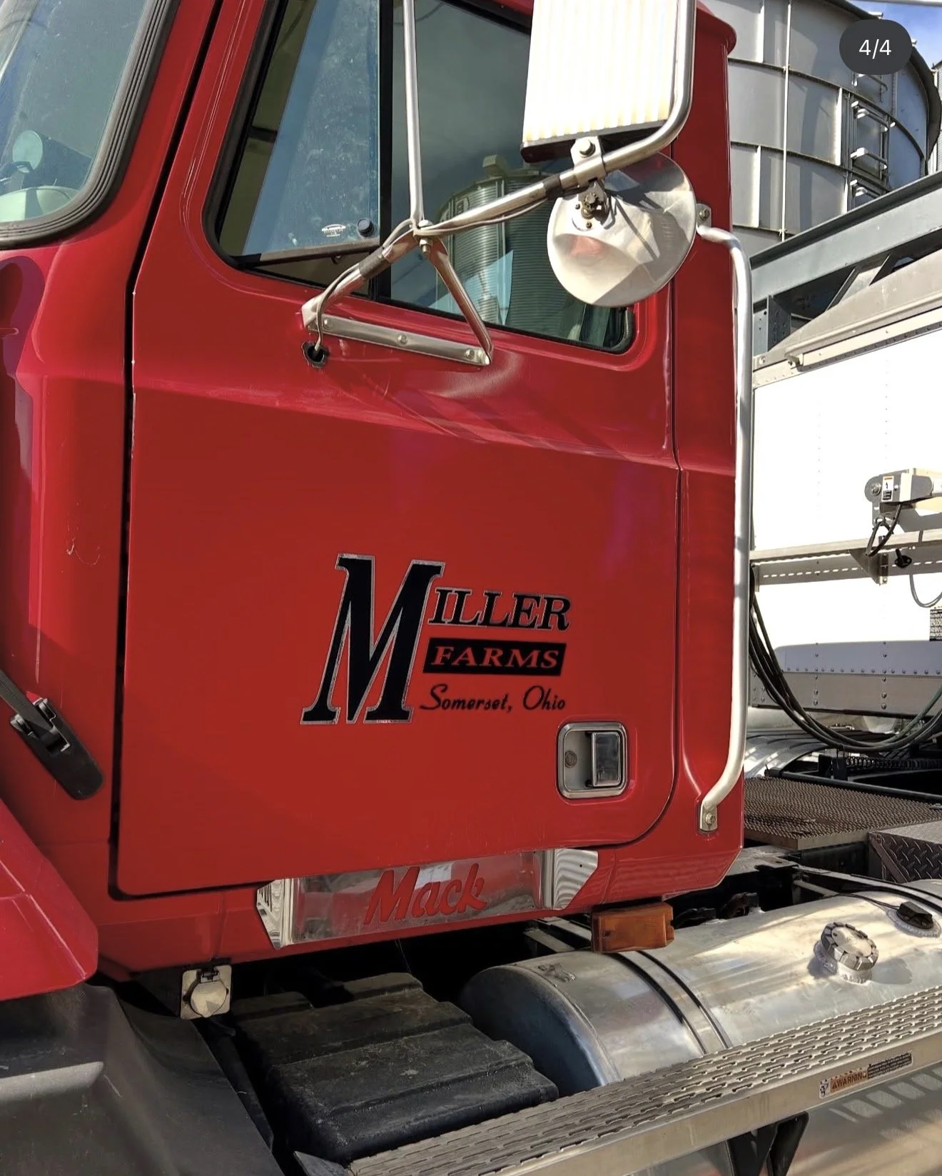 Close-up of a red truck with a label that reads 'Miller Farms, Somerset, Ohio.' The truck has a side mirror and a window, with a metal ladder and some equipment visible on the side.