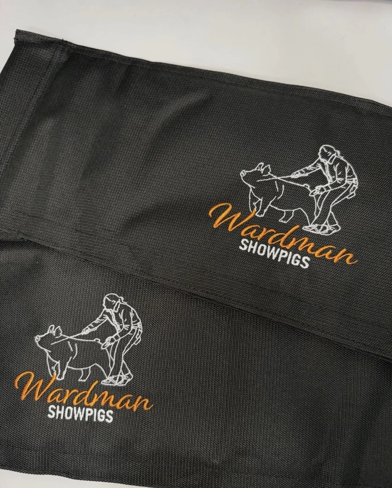A black showpig show bag with a logo of a person riding a pig embroidered in white, and the text 'Wardman SHOWPIGS' embroidered in orange and white.