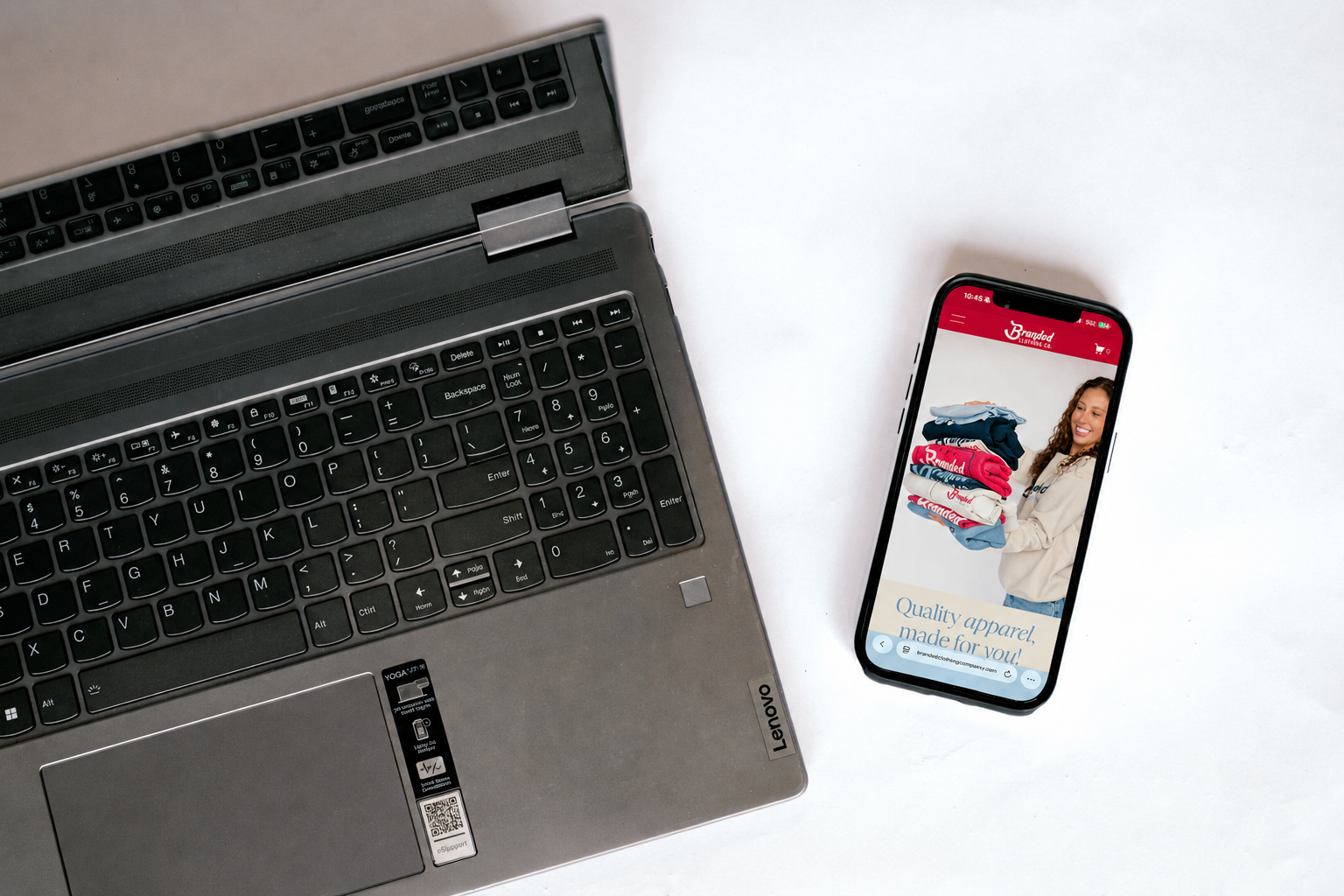 A laptop computer and a smartphone displaying an online clothing store with a woman holding folded apparel on the screen.