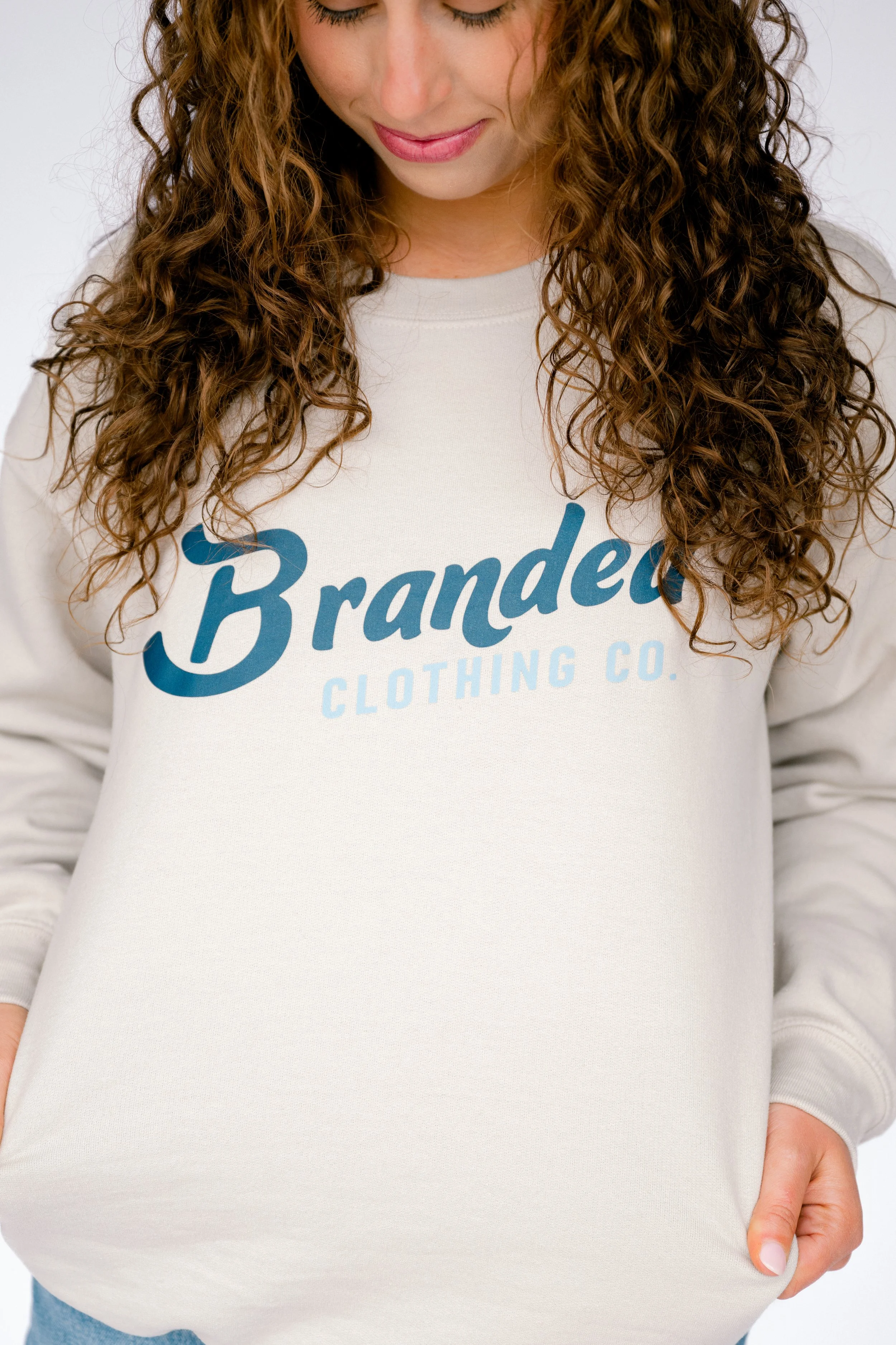 Close-up of a woman with curly brown hair wearing a white sweatshirt that has the word 'Branded' printed on it.
