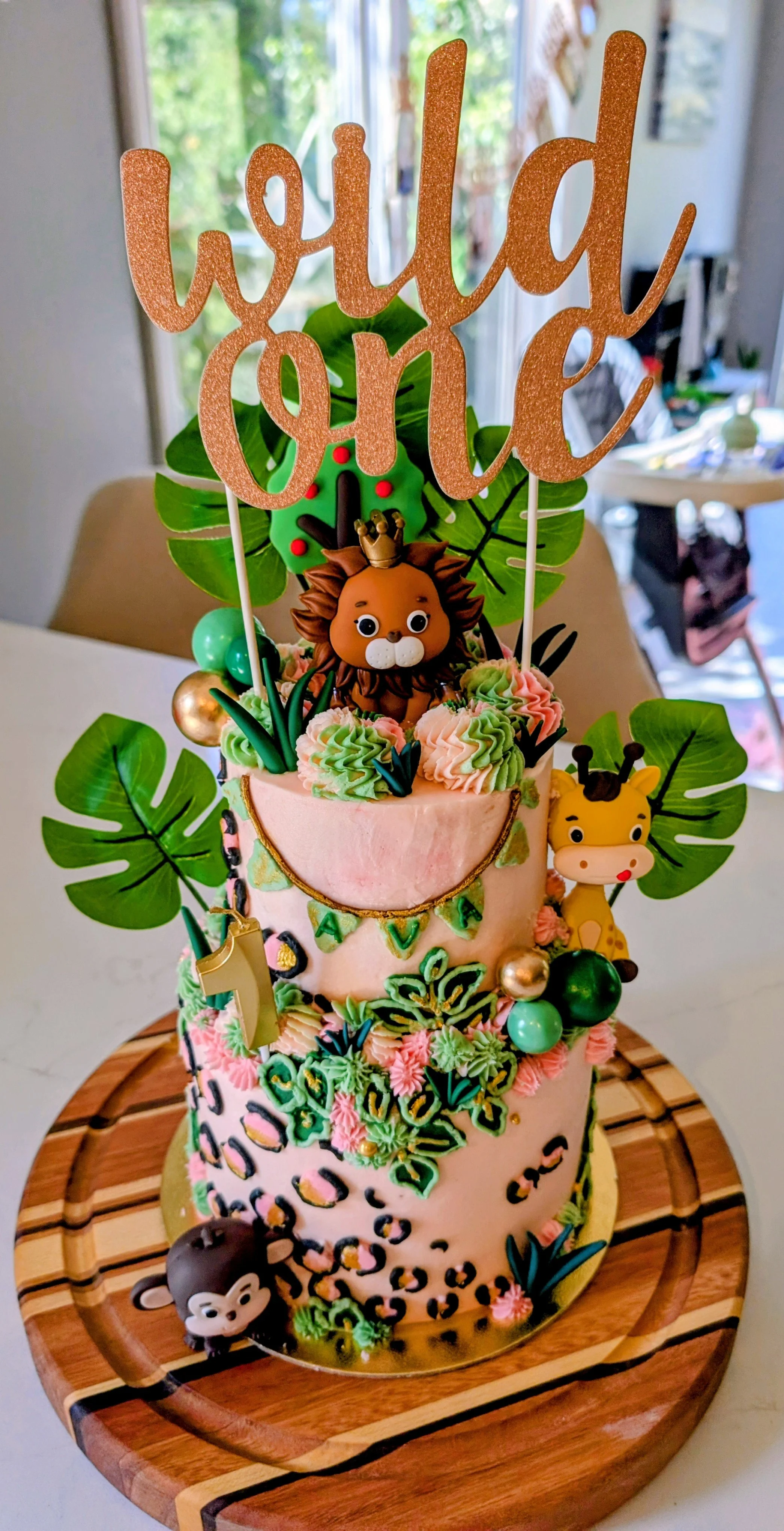 Colorful jungle-themed birthday cake with animal decorations, green leaves, and a 'hello love' topper, on a wooden cake board.