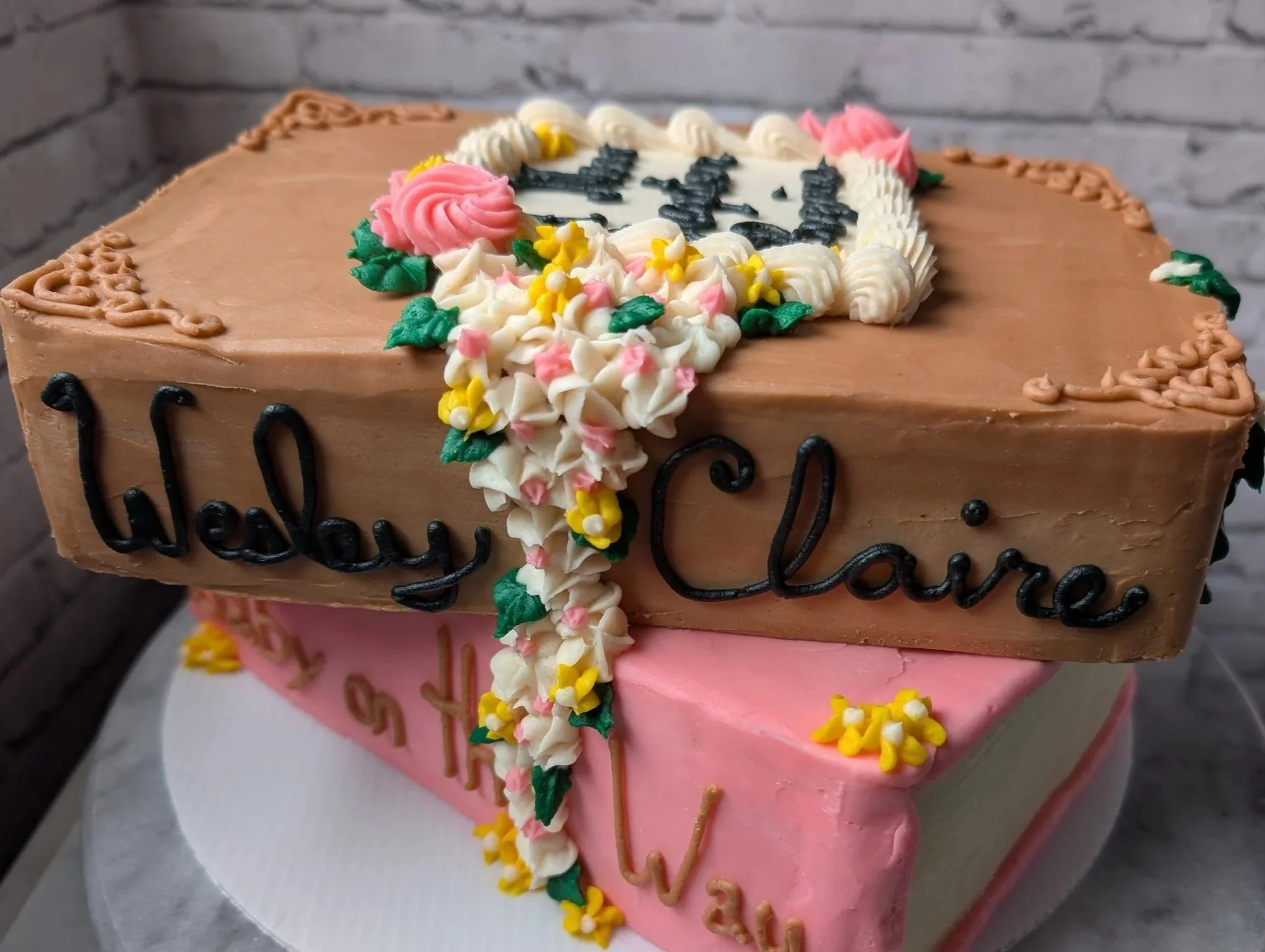 Two layered heart-shaped birthday cake with pink and brown frosting, decorated with flowers and a message that says 'Happy Birthday.'
