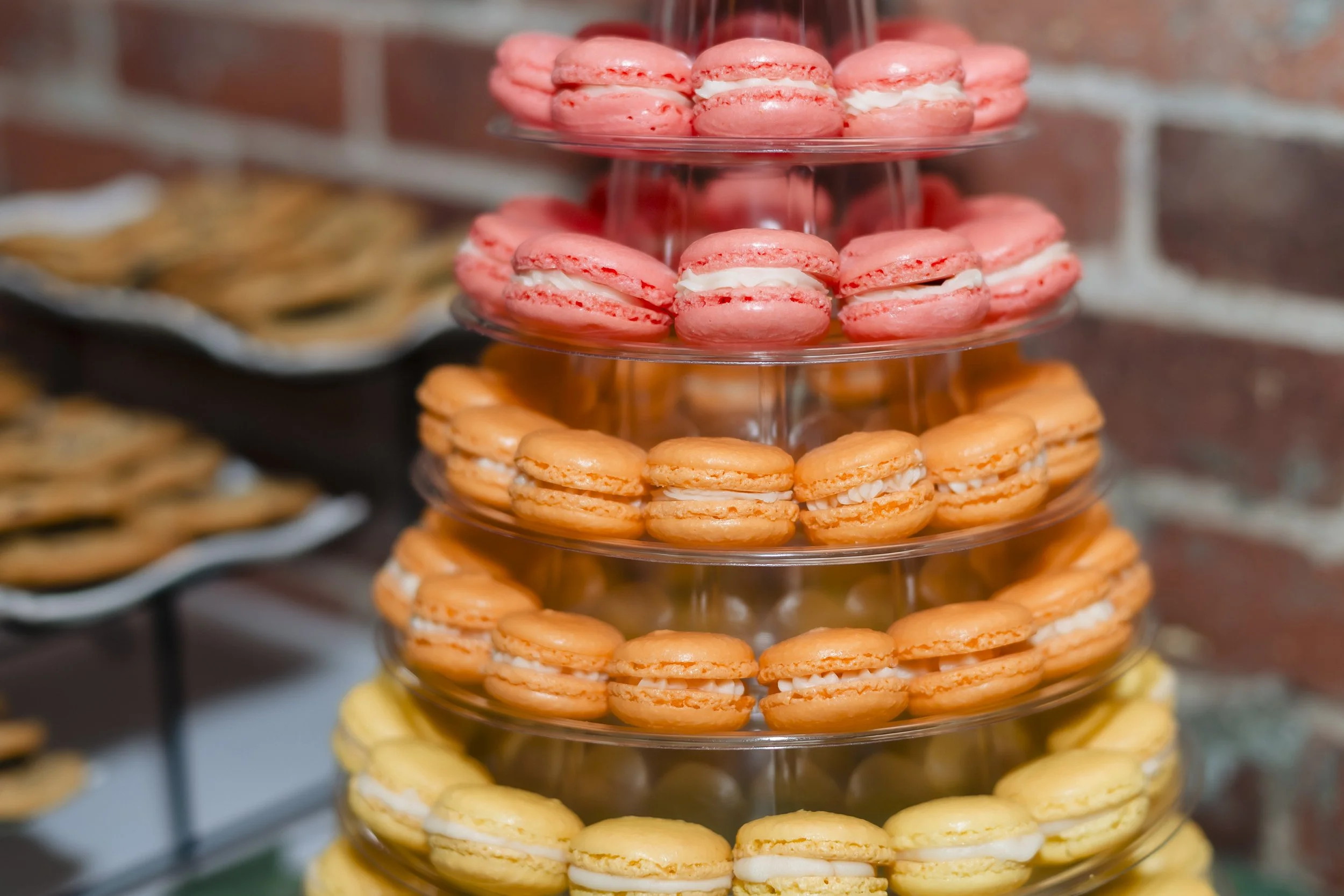 Stacked tiered tray filled with pink, orange, and yellow macarons.