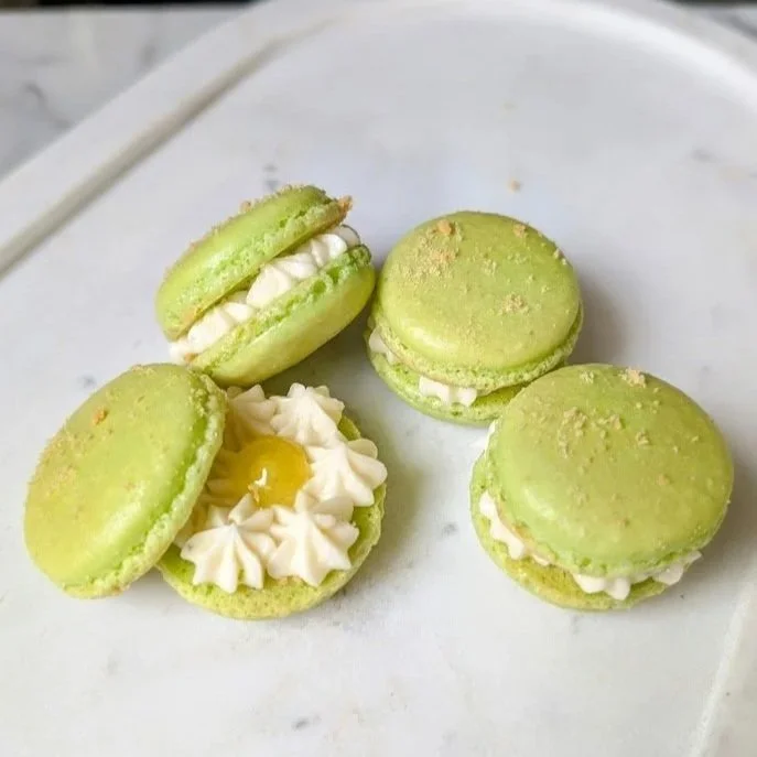 Four green macarons with white filling, one filled with yellow jam or lemon curd, on a white plate.