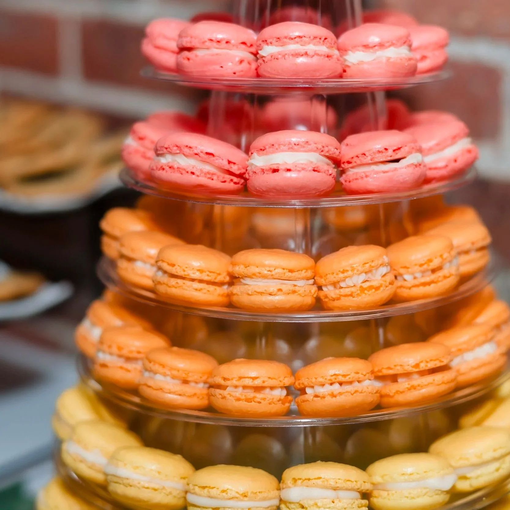 Tiered stand filled with pink, orange, and yellow macarons at a dessert display.