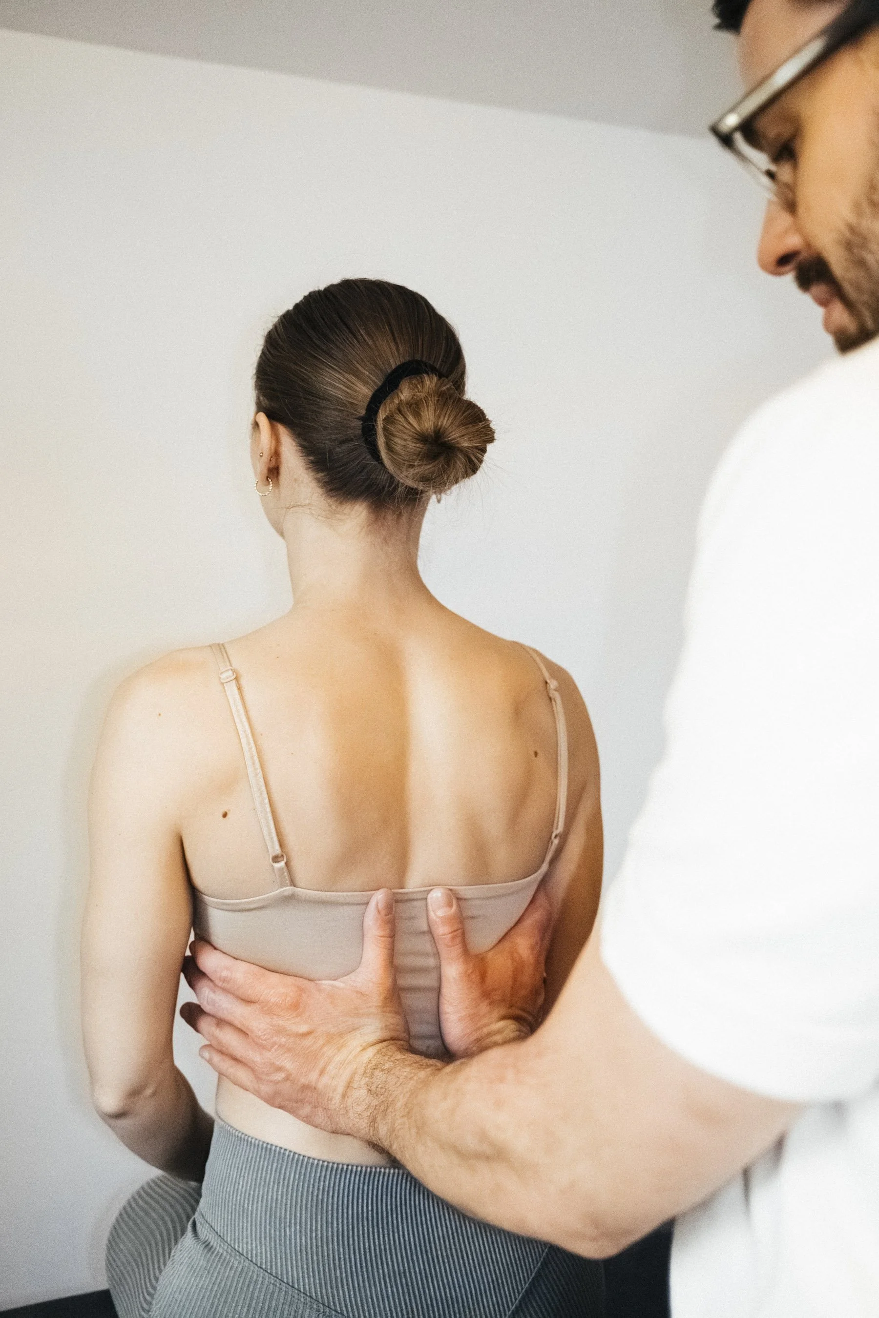 Ein Mann führt eine chiropraktische Untersuchung an einer Frau durch, die mit dem Rücken zur Kamera sitzt, während sie sich leicht nach vorne neigt.