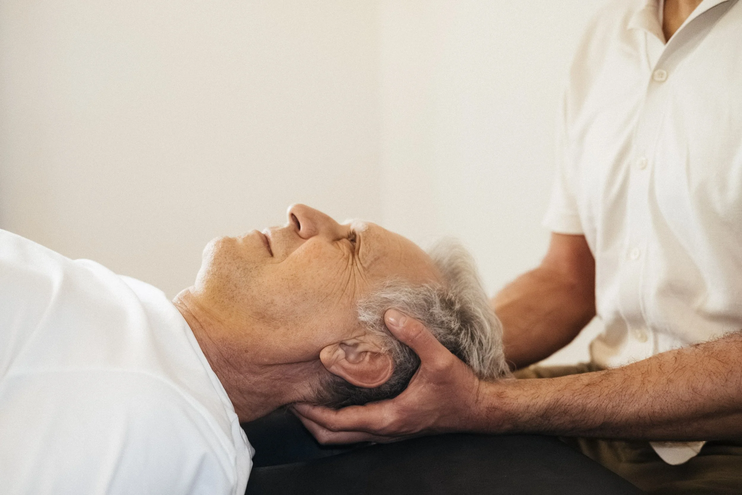 Ein älterer Mann liegt mit geschlossenem Gesicht auf einer Liege, während eine Person ihn an einem Therapiegerät hält.
