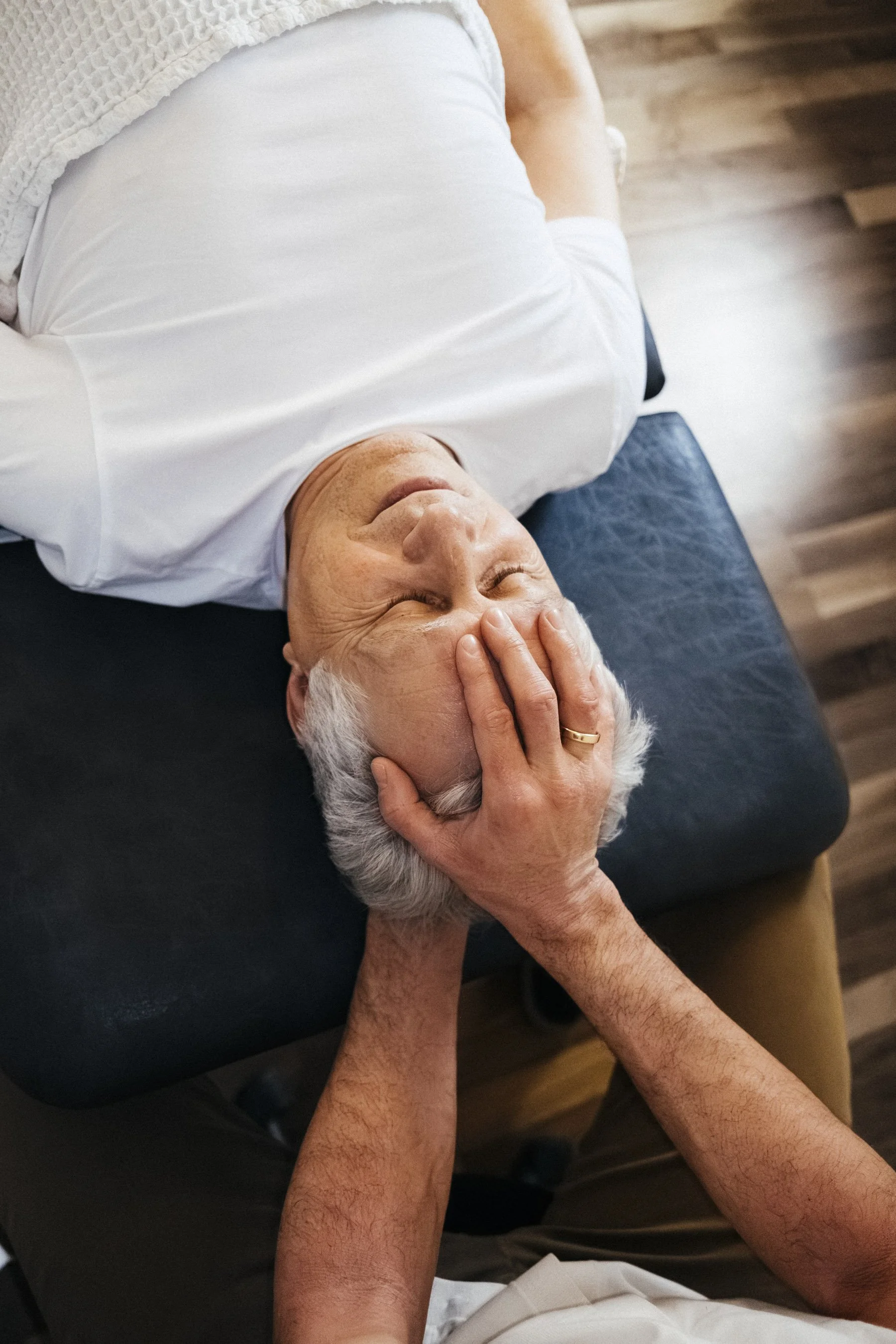 Ein älterer Mann liegt entspannt auf einer Couch, während jemand seine Kopf mit den Händen hält und sanft massiert.