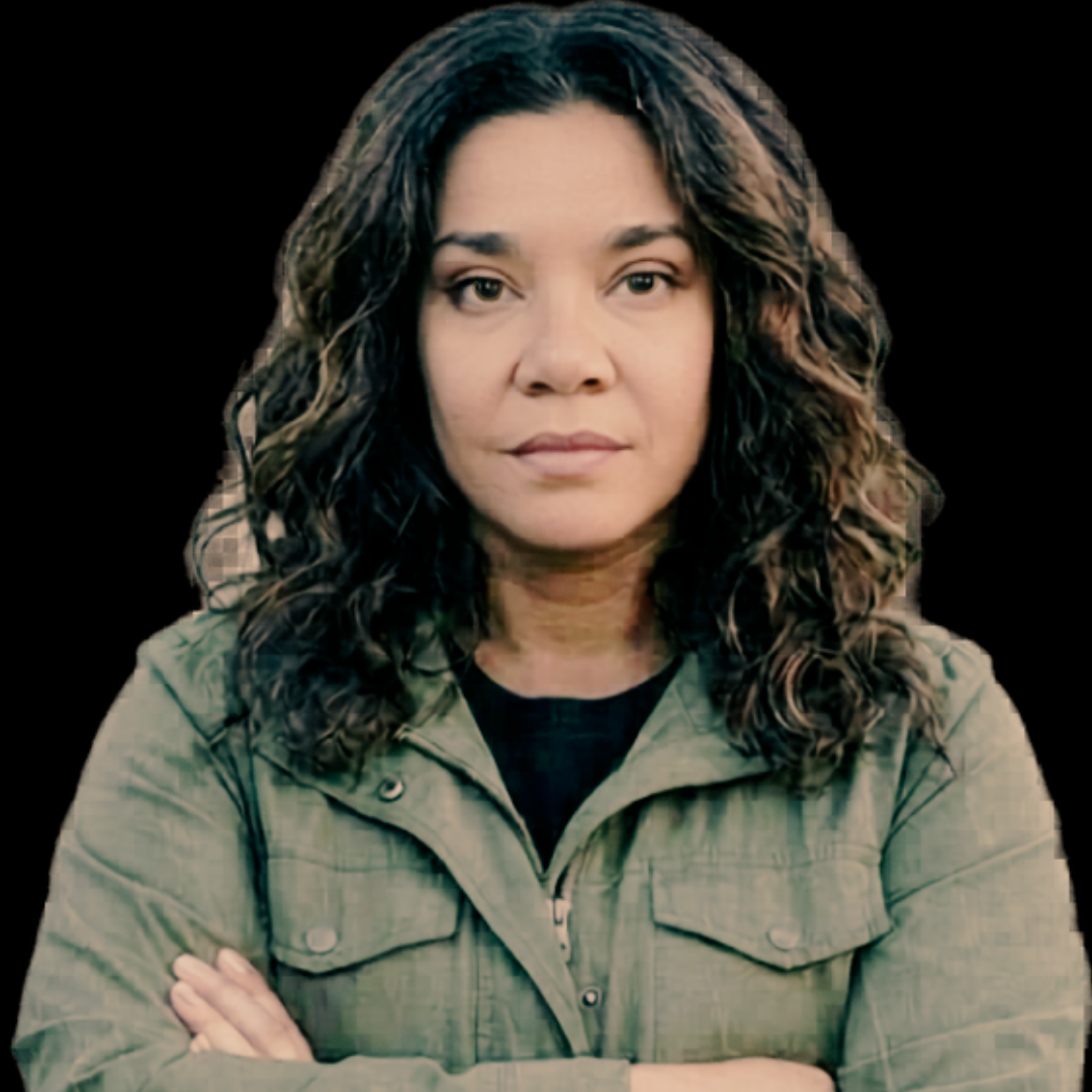 Lynn Jordan, the Urban Lady Prepper. Curly brown hair, wearing a green jacket, facing forward with arms crossed against a black background.