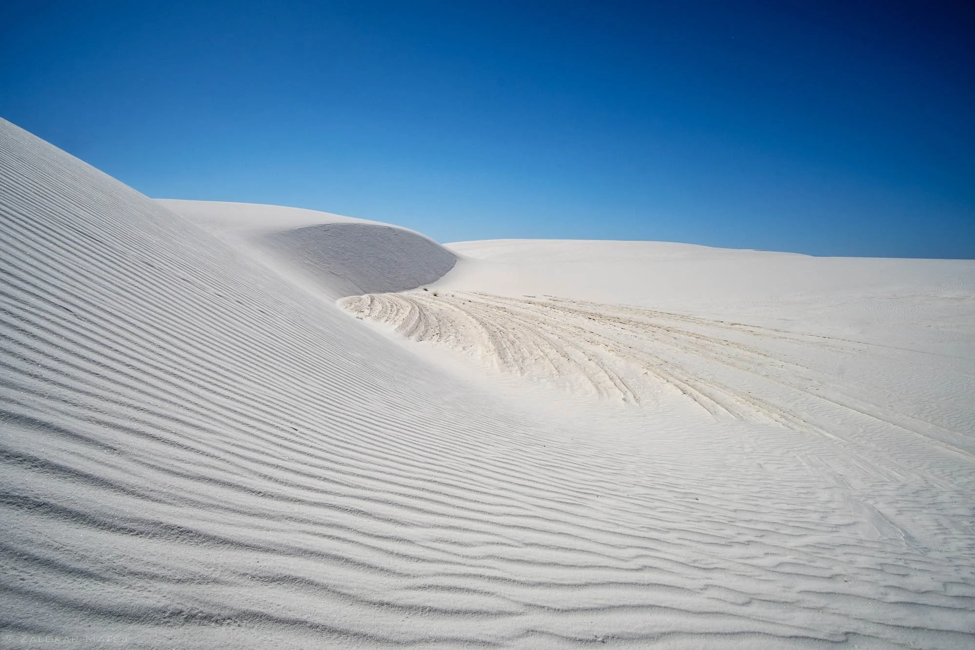 A desert landscape with white sand dunes and clear blue sky.