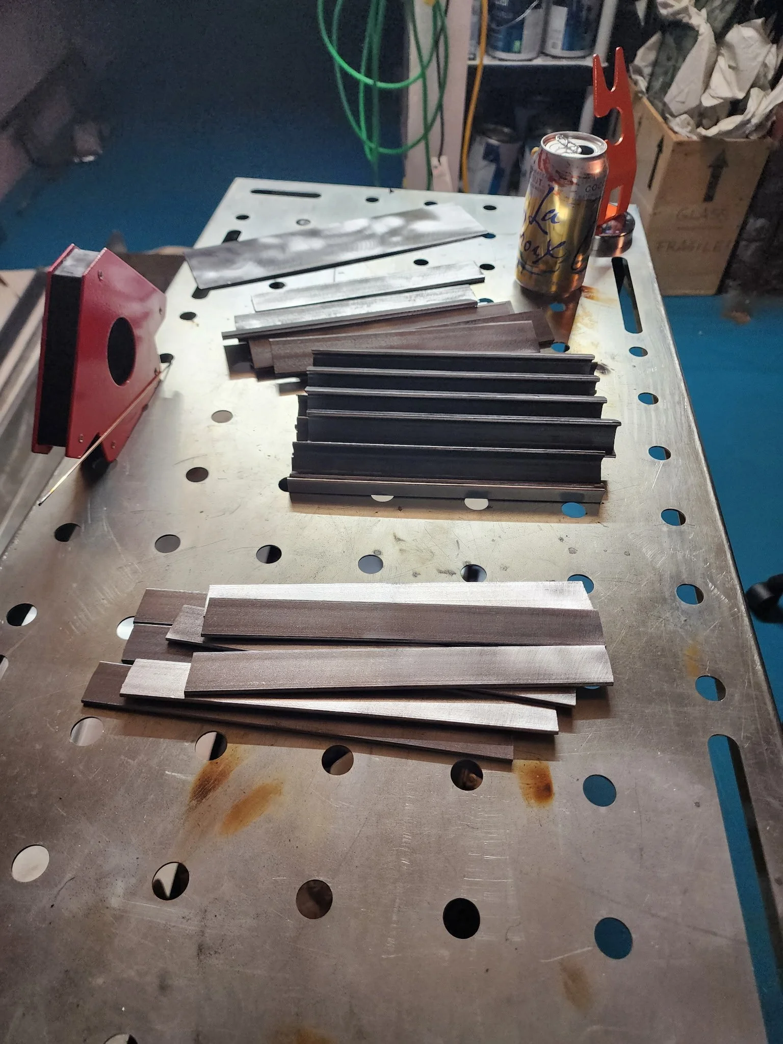 Metal pieces arranged on a workbench in a workshop, with a soda can and tools in background.