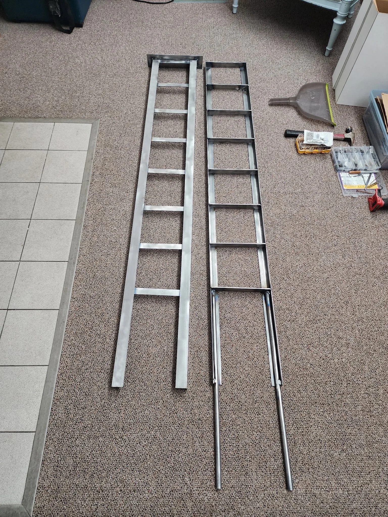Two metal ladders placed on a carpeted floor in a room with various tools and storage boxes around.