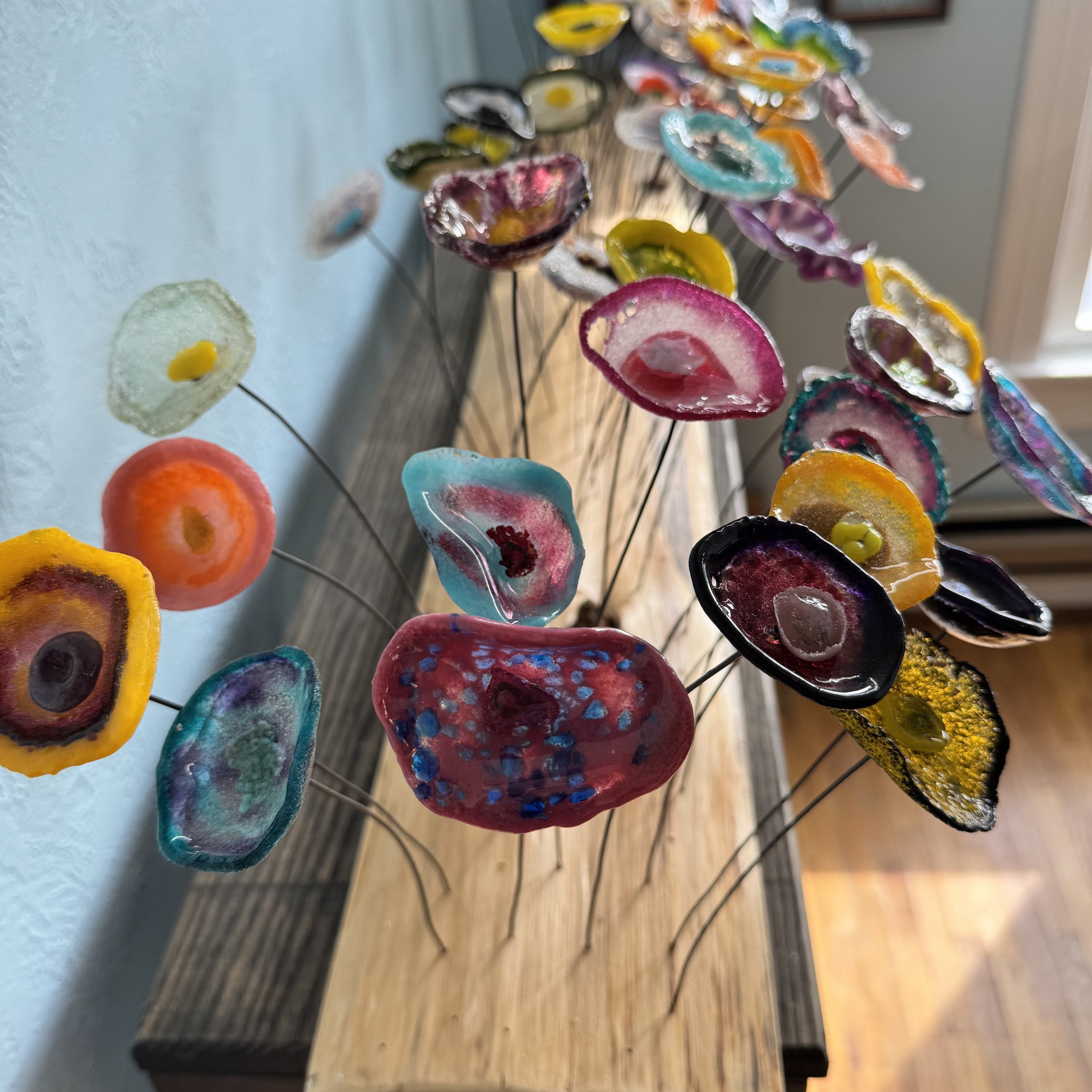 Colorful glass art flowers arranged on a wooden table.