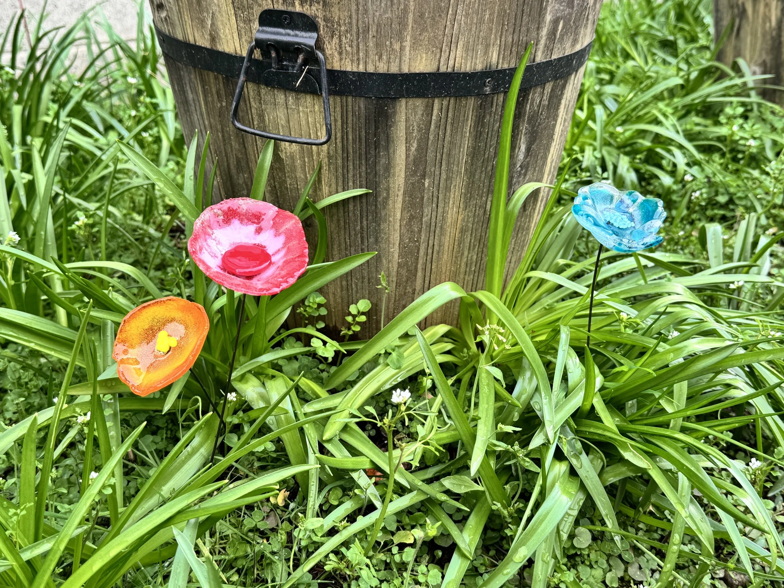 Colorful glass flowers in a garden near a wooden post.