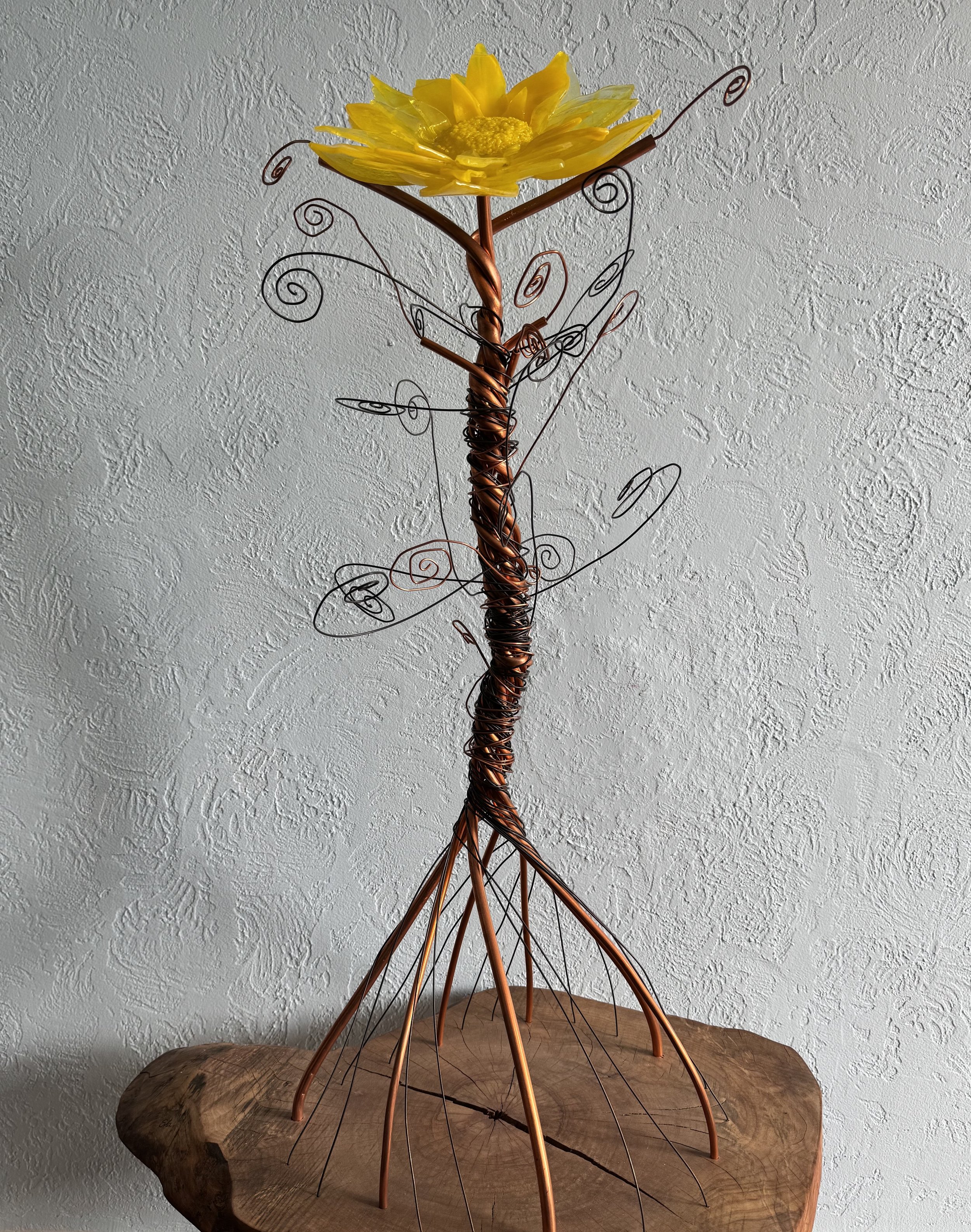 Decorative metal sculpture resembling a flower with a yellow petal top, mounted on a wooden base.