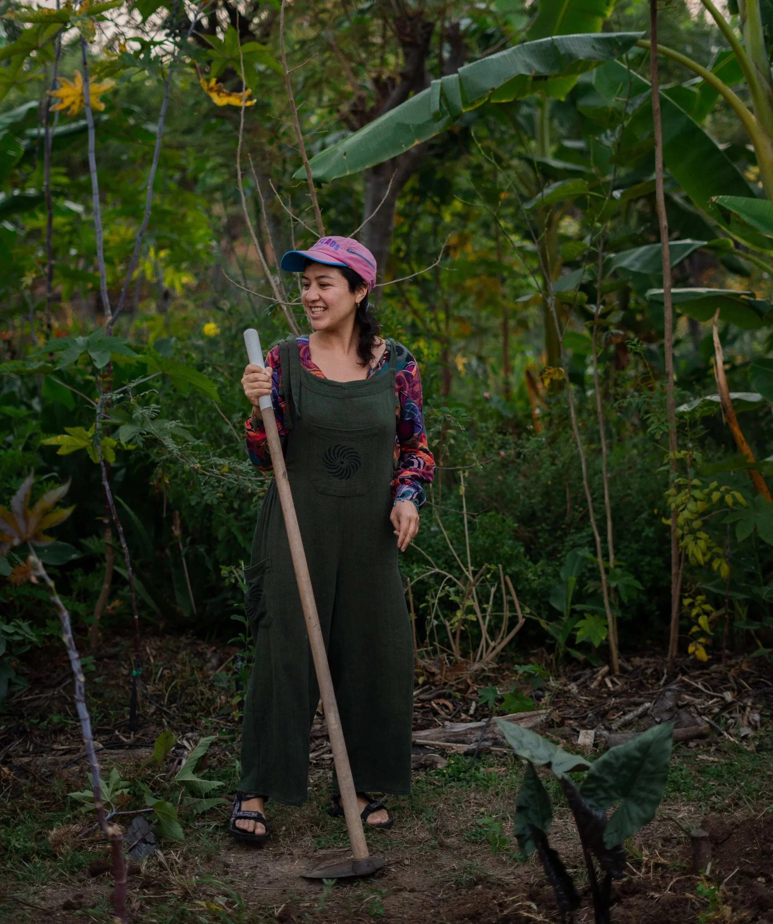 Mujer en taller práctico durante un programa de aprendices de permacultura y agricultura regenerativa trabajando cultivo con azada en entorno natural tierra del sol oaxaca