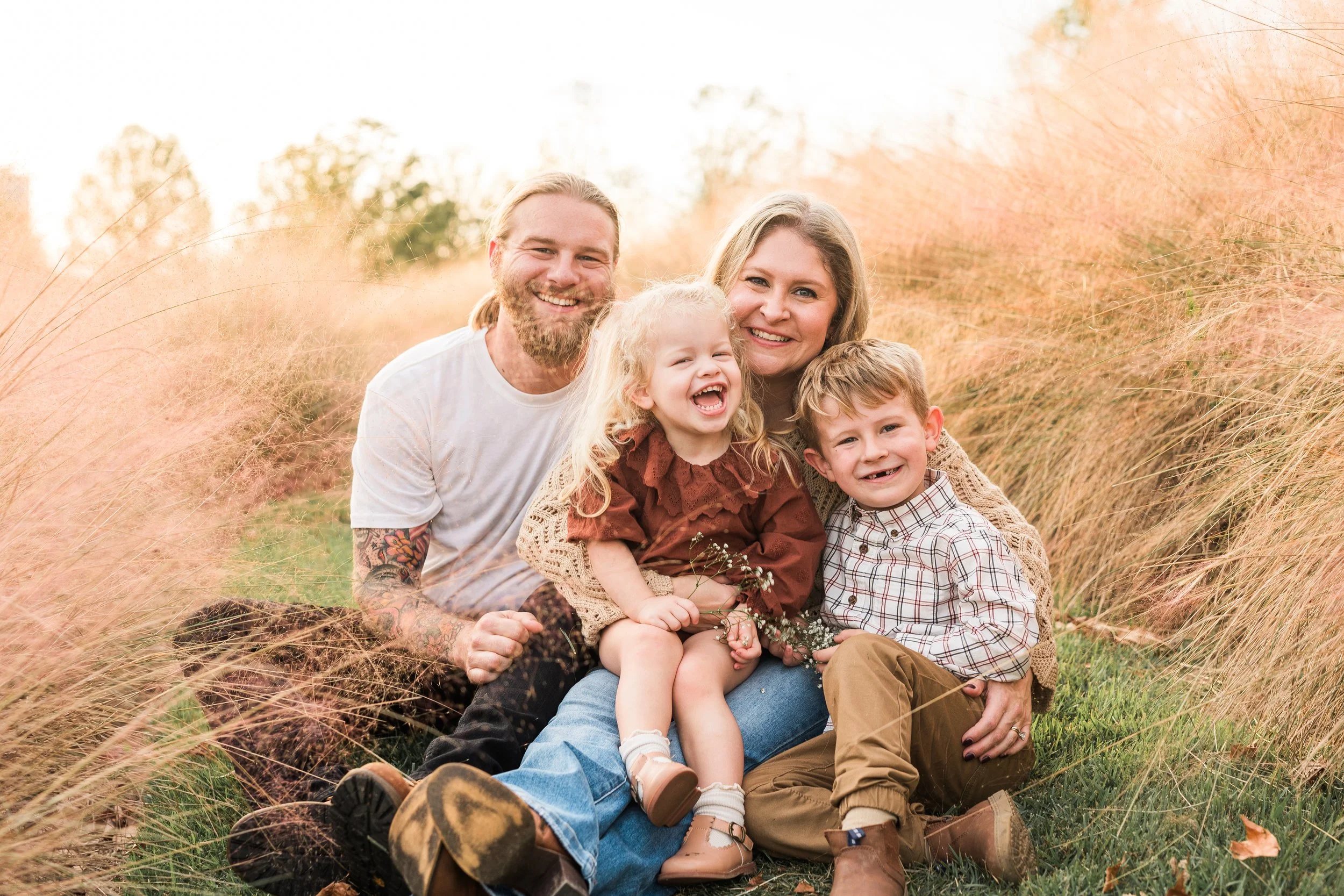 Railroad Park, Downtown Birmingham, AL - A happy family of four sitting outdoors among tall grass, smiling and laughing at the camera during the daytime.