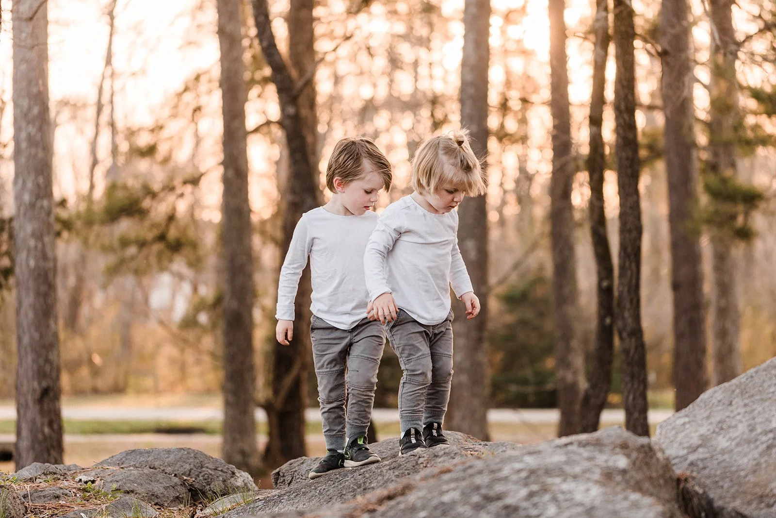 Leeds, AL - Two young boys, walking on rocks in a wooded area during sunset.