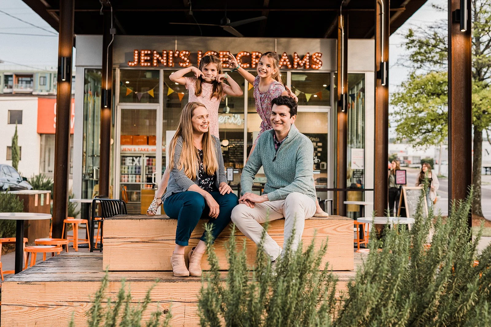 Pepper Place, Downtown Birmingham, AL - A family of four sitting outside a dessert shop called 'Jeni's Ice Creams.' The family has two young girls on top, making funny faces, and a man and woman sitting on a wooden bench, smiling.