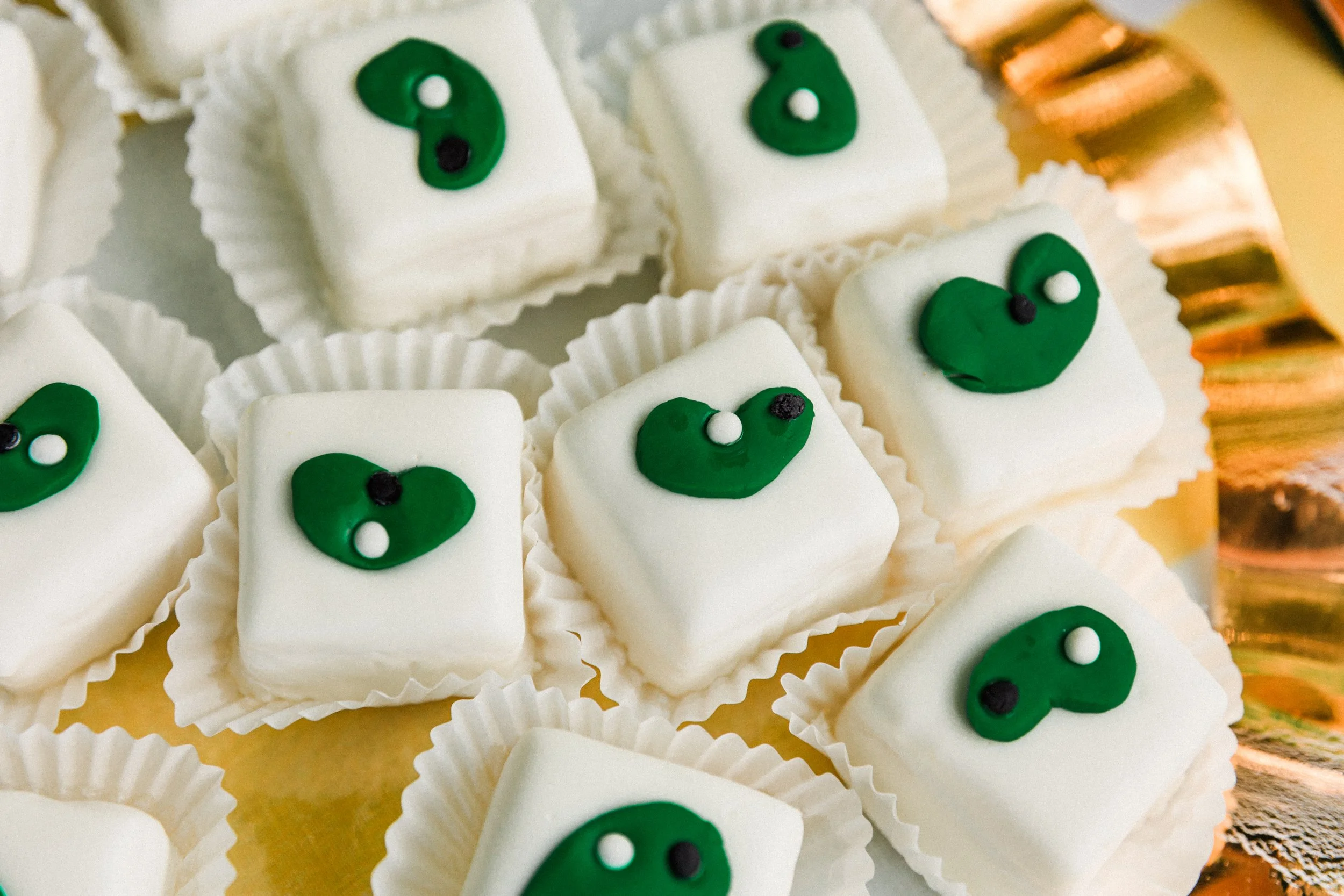 Mountain Brook, AL - Petit fours decorated with green and black icing, placed in white paper cups.