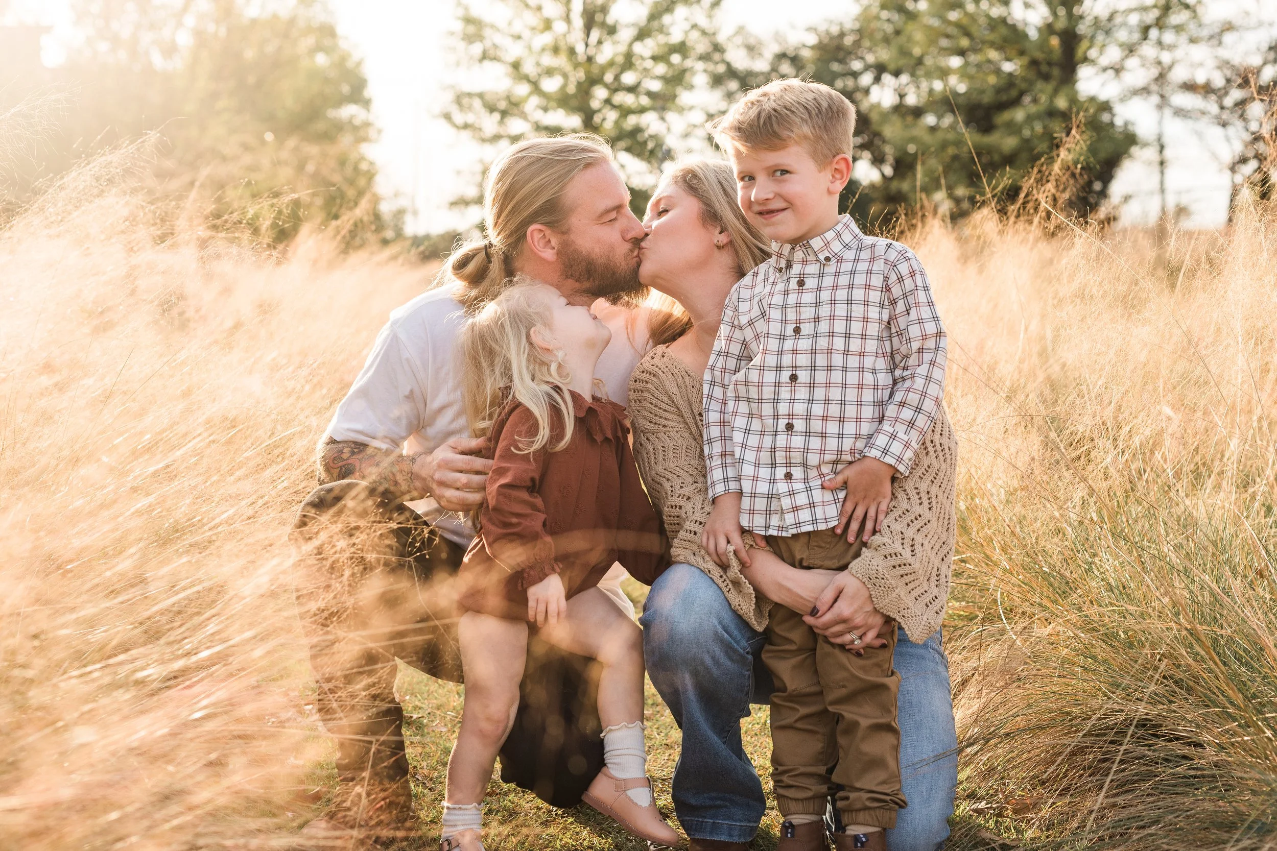 Railroad Park, Birmingham, AL - A family of four in a field of tall, golden grass, sharing a moment with a kiss and smiles during sunset.