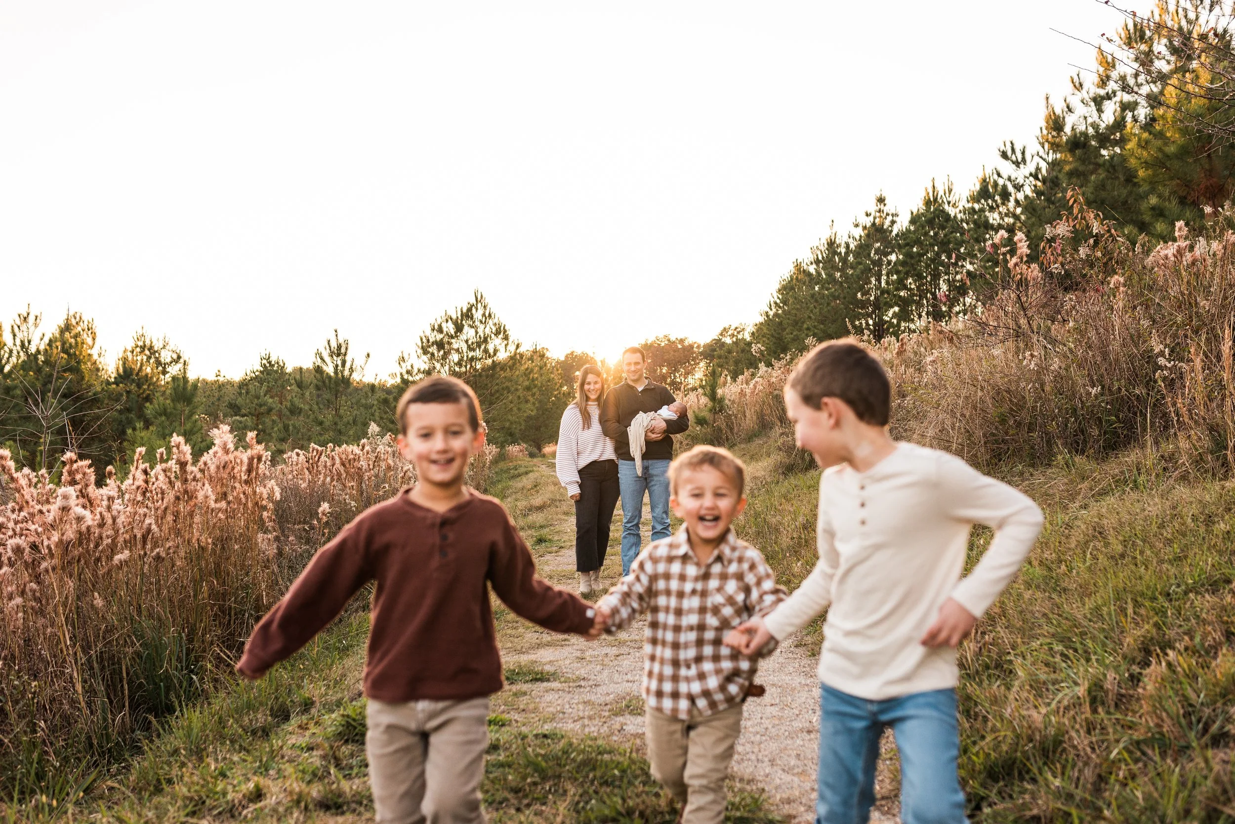 Sicard Hollow, Vestavia, AL -A family of six enjoying a walk outdoors on a dirt trail during sunset, with three young boys in the foreground and parents carrying a baby in the background.