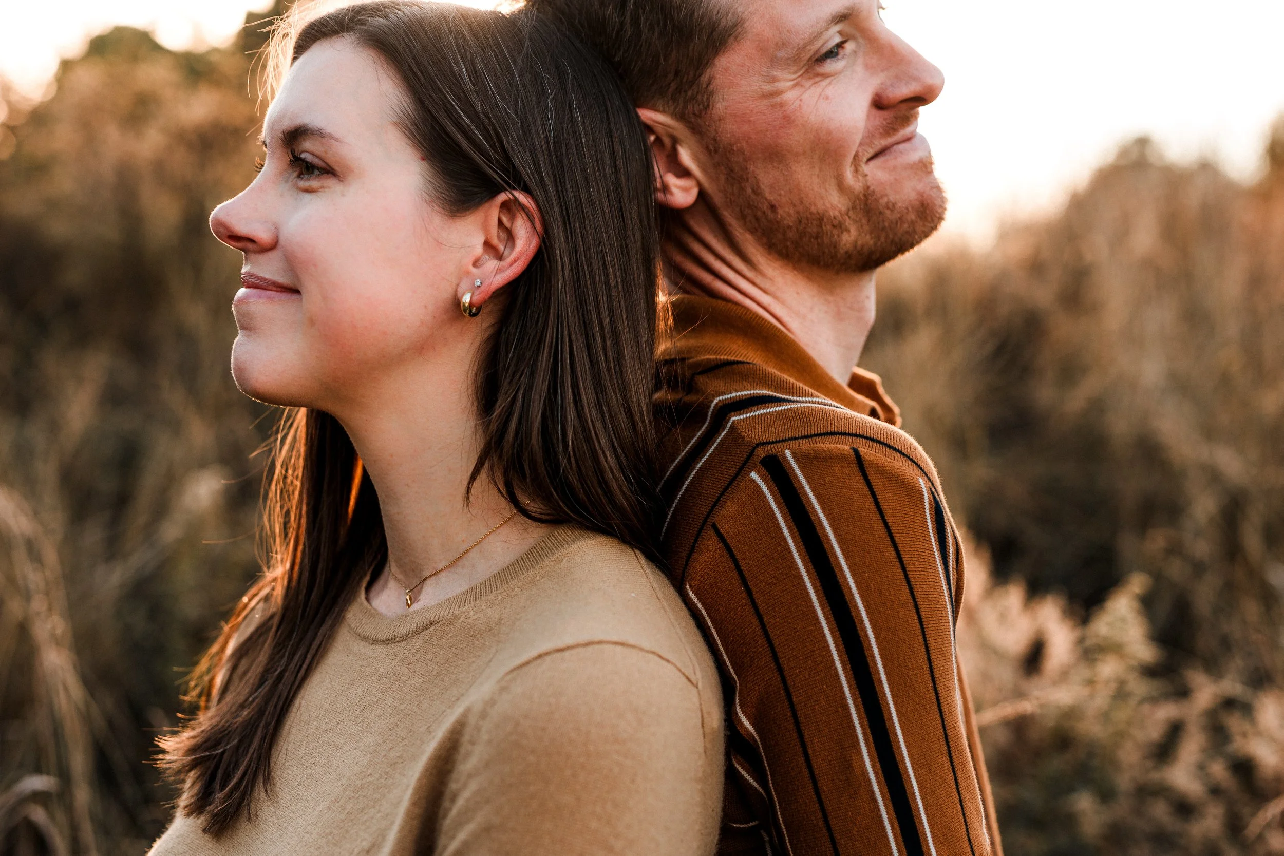 Vestavia, AL - A young woman and a man are standing back-to-back outdoors during sunset, both with peaceful smiles, facing opposite directions.