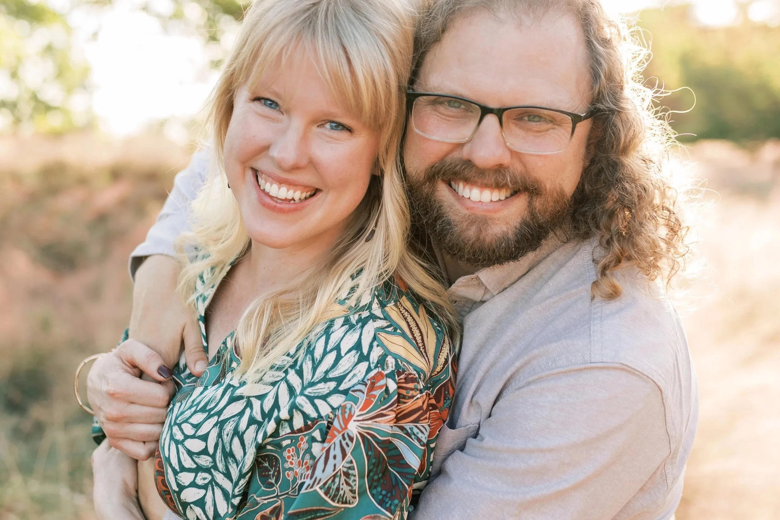 Railroad Park, Downtown Birmingham, AL - A smiling couple outdoors, embracing each other with a blurred natural background.