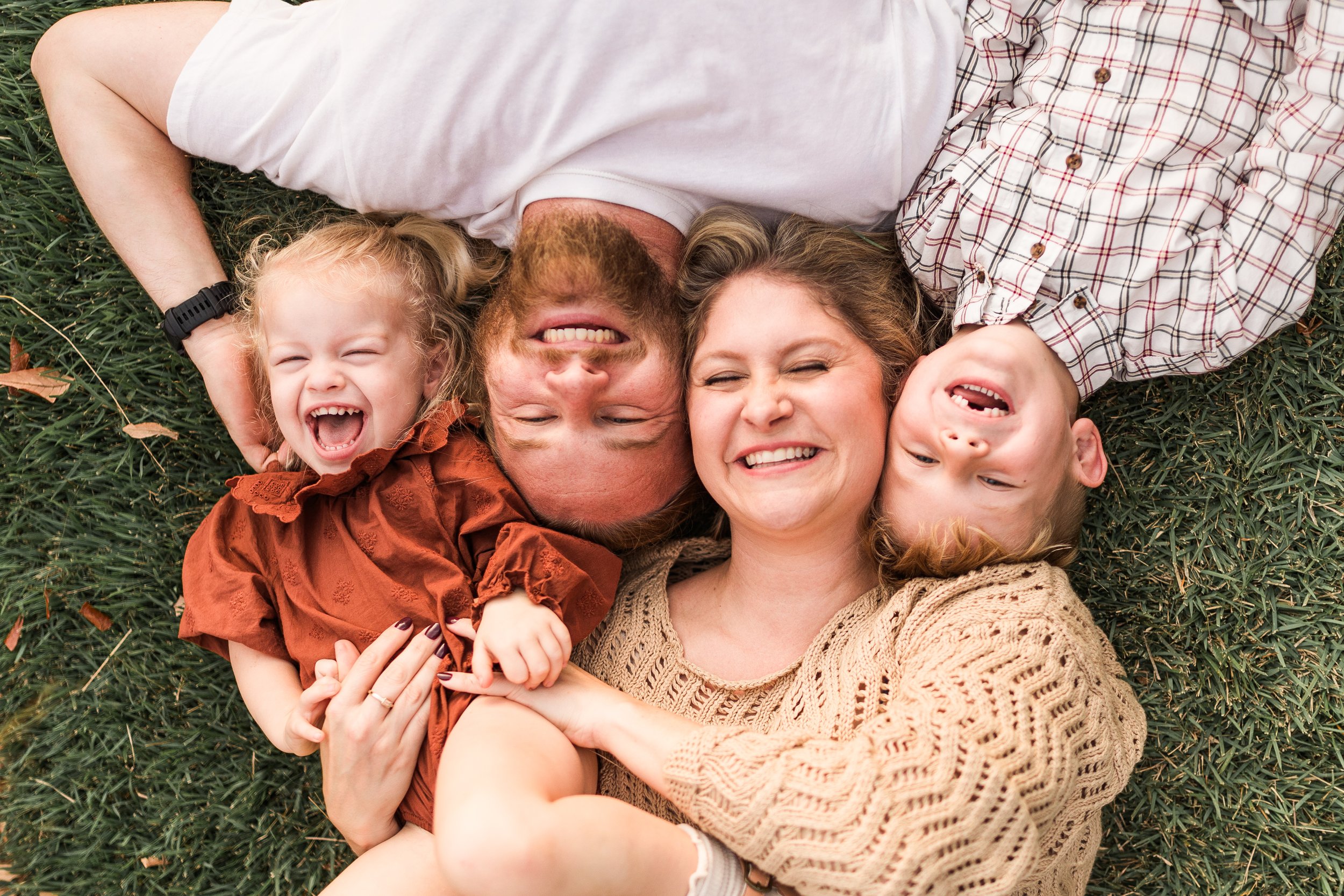 Railroad Park, Downtown Birmingham, AL - A family of four lying on the grass, smiling and laughing together, looking up at the camera.