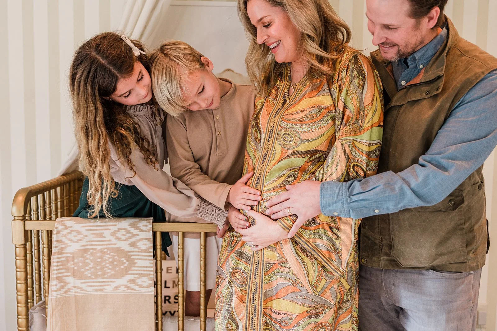 Mountain Brook, AL - A family gathered around a pregnant woman, touching her belly and smiling in a warmly lit room.