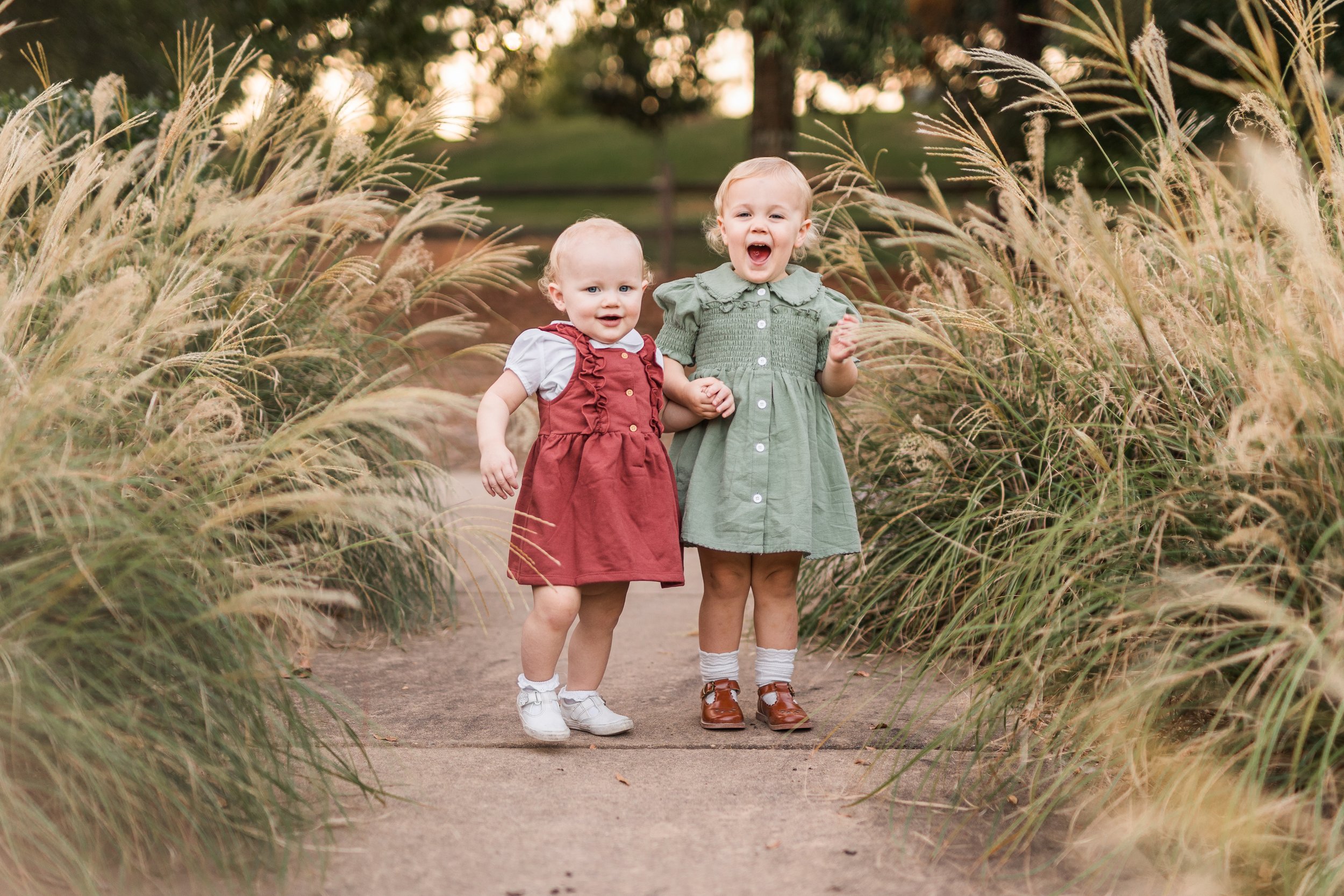 Vestavia, AL - Two young girls walking hand in hand on a dirt path surrounded by tall grasses, smiling and enjoying outdoors.