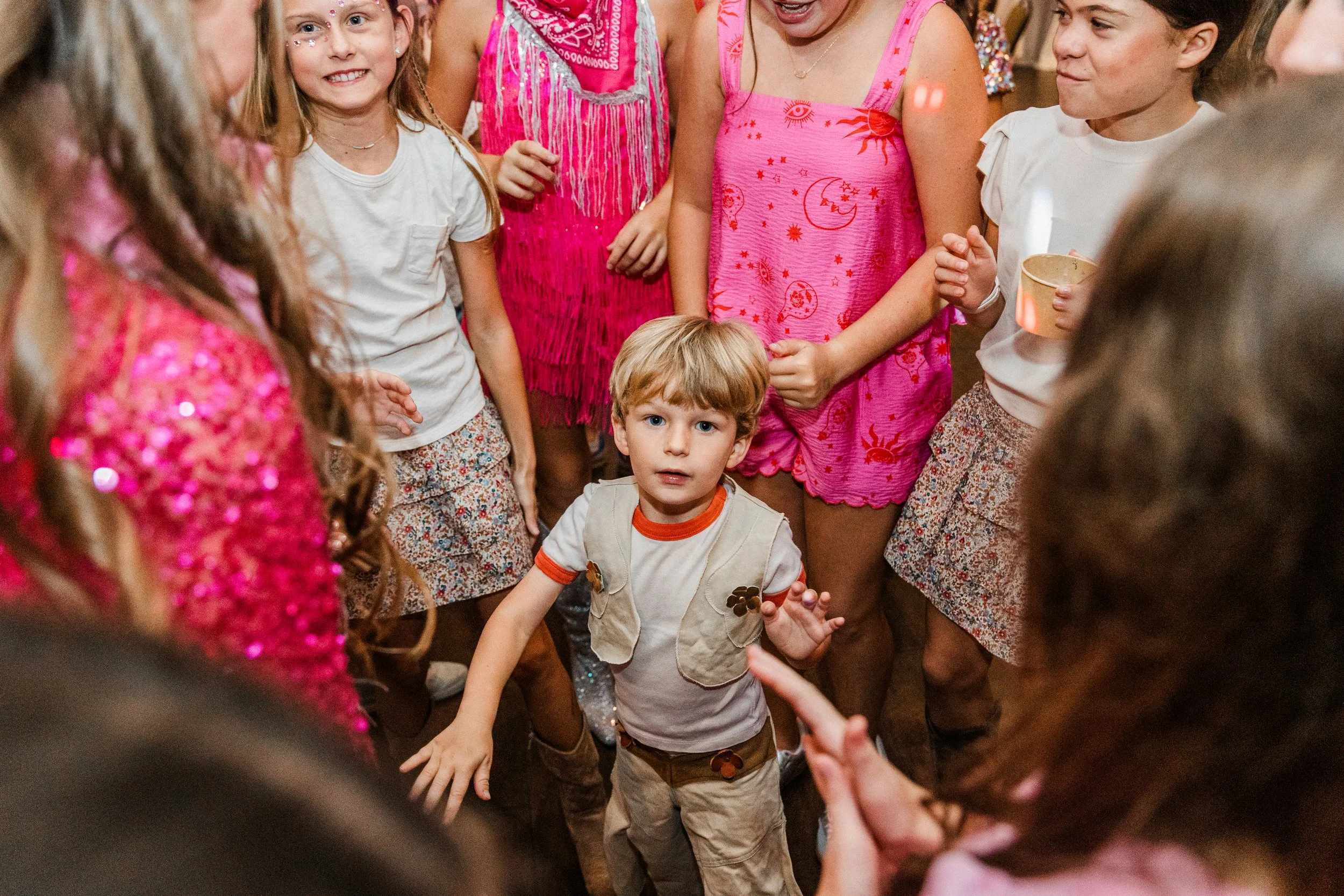 Mountain Brook, AL - Children gathered and dancing around a young boy with blonde hair in a beige vest and white T-shirt, at a party.