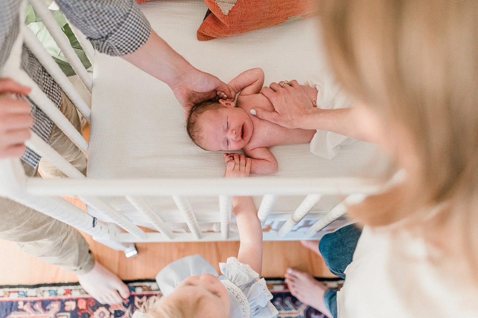 Gadsden, AL - A newborn baby lying in a crib, with a person holding the baby's head and another person touching the baby's chest, during a newborn session.