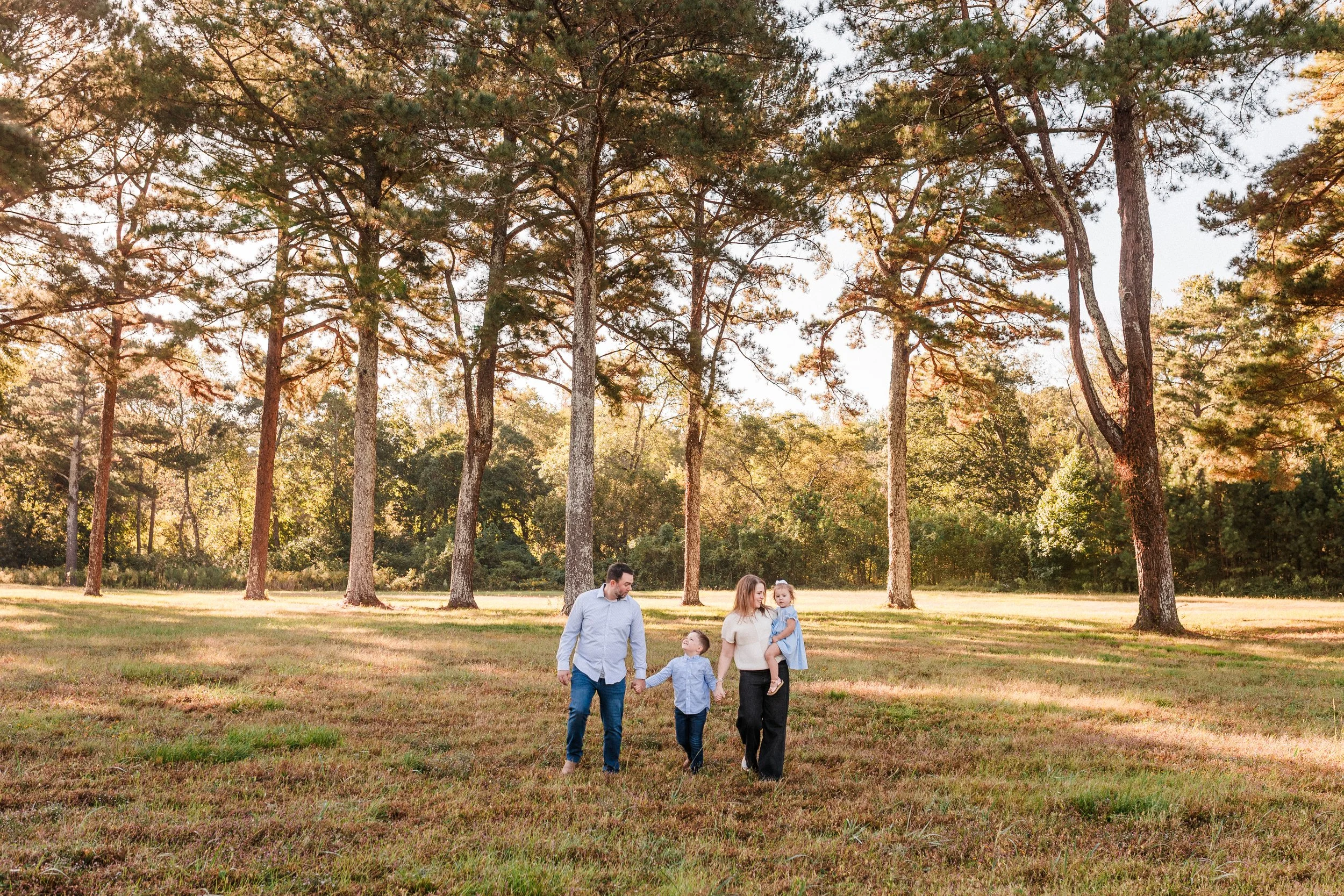 Vestavia, AL -Family of four walking together in a park with tall trees and green grass during late afternoon or early evening.