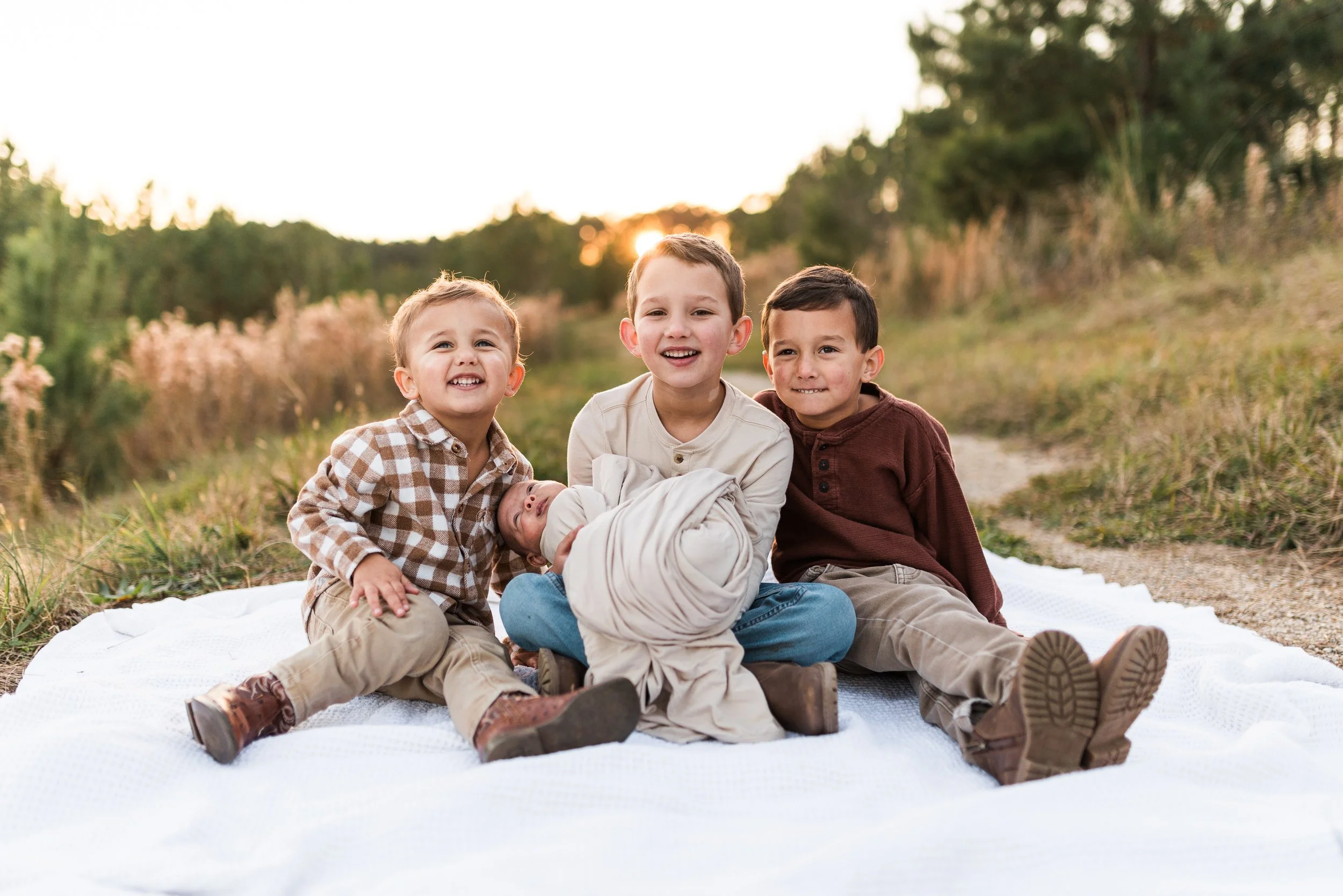 Sicard Hollow, Vestavia, AL - Four children sitting on a white blanket in a field during sunset, with one baby wrapped in a swaddle.