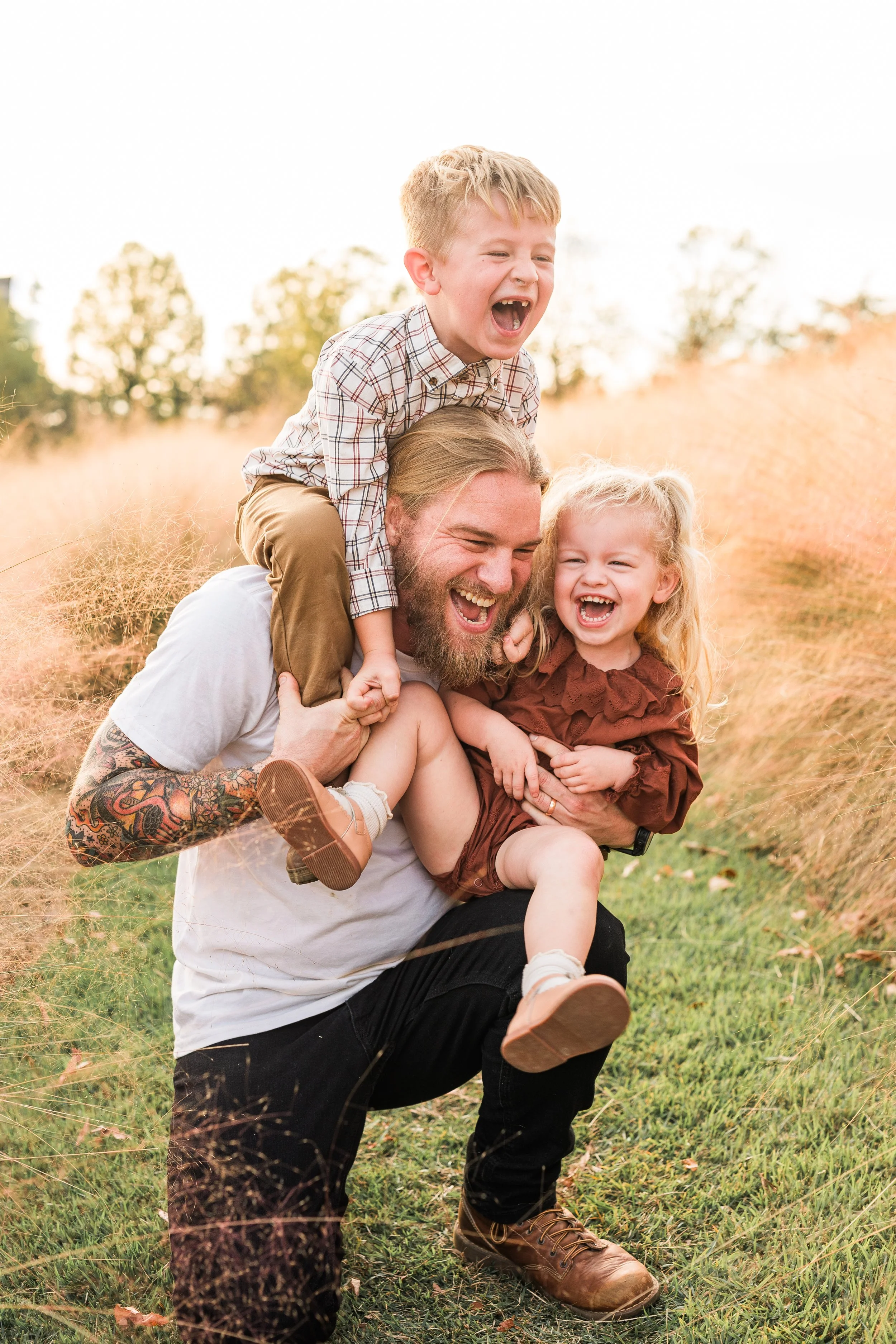 Railroad Park, Downtown Birmingham, AL - A man playing with two children outdoors in a field of tall grass, all three are laughing and having fun.