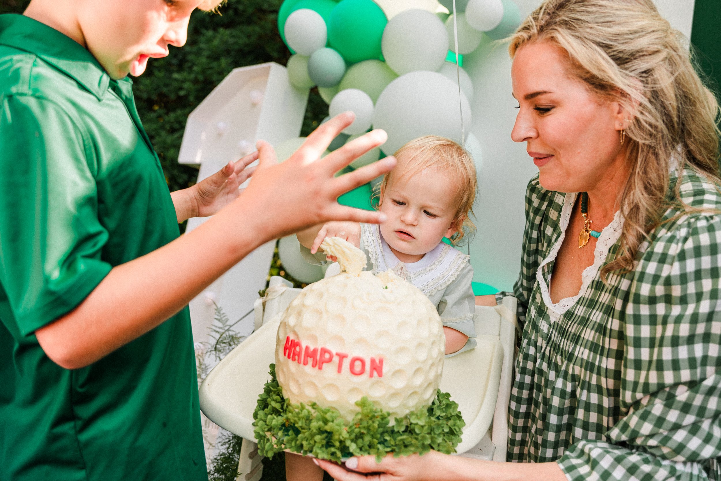 Mountain Brook, AL - A young boy in a green shirt is celebrating a birthday with a cake shaped like a golf ball that has 