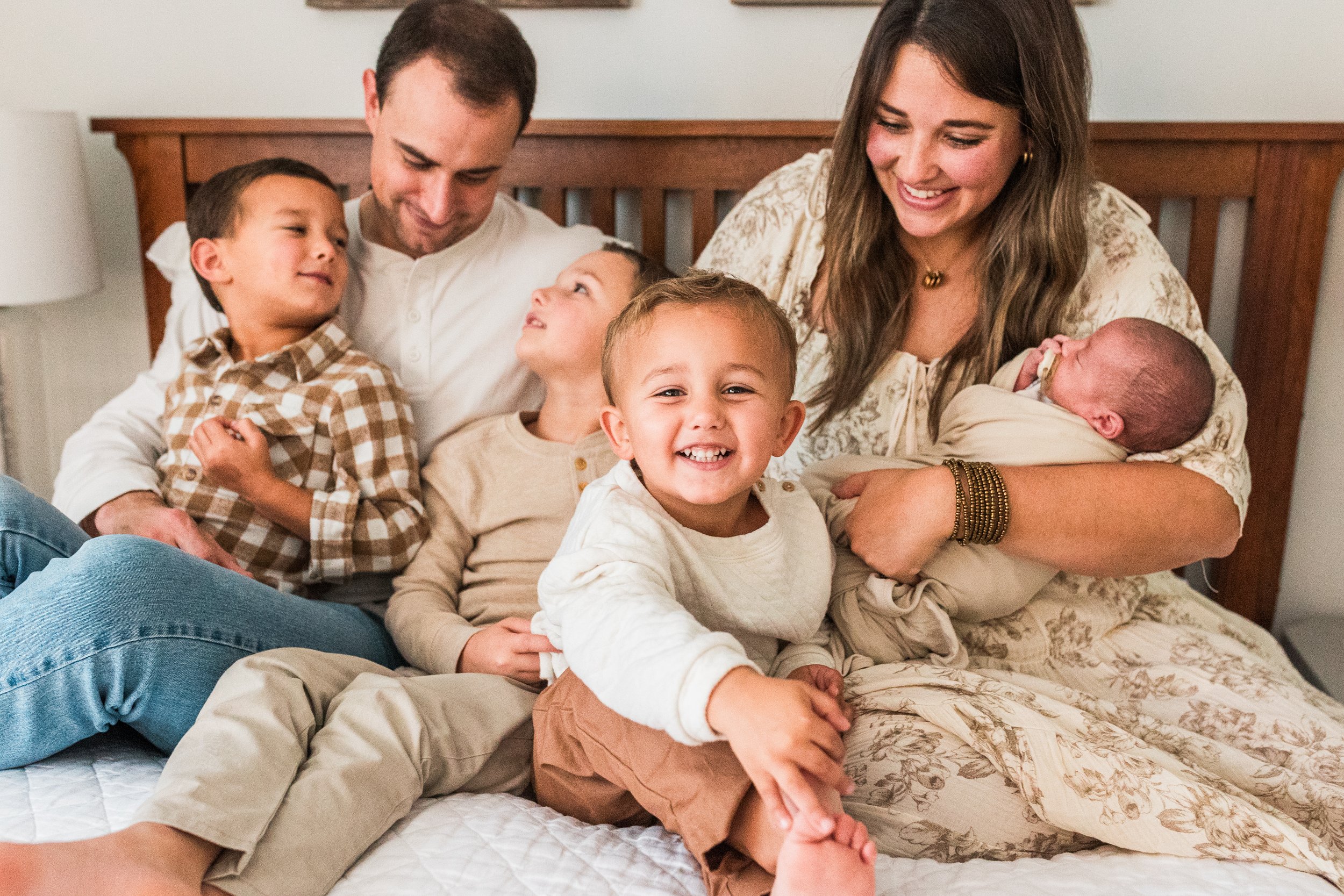 Hoover, AL - A happy family sitting on a bed, including two adults and four children, one of whom is a newborn being held by a woman. Everyone is smiling and looking at each other.