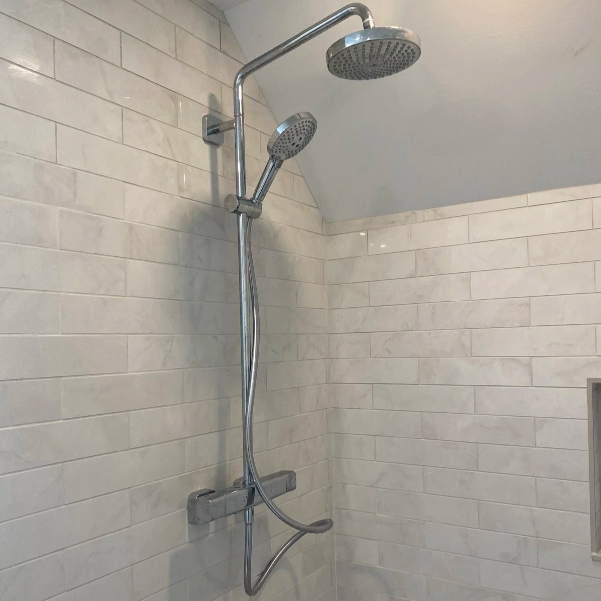 Shower with dual showerheads and white tiled wall.