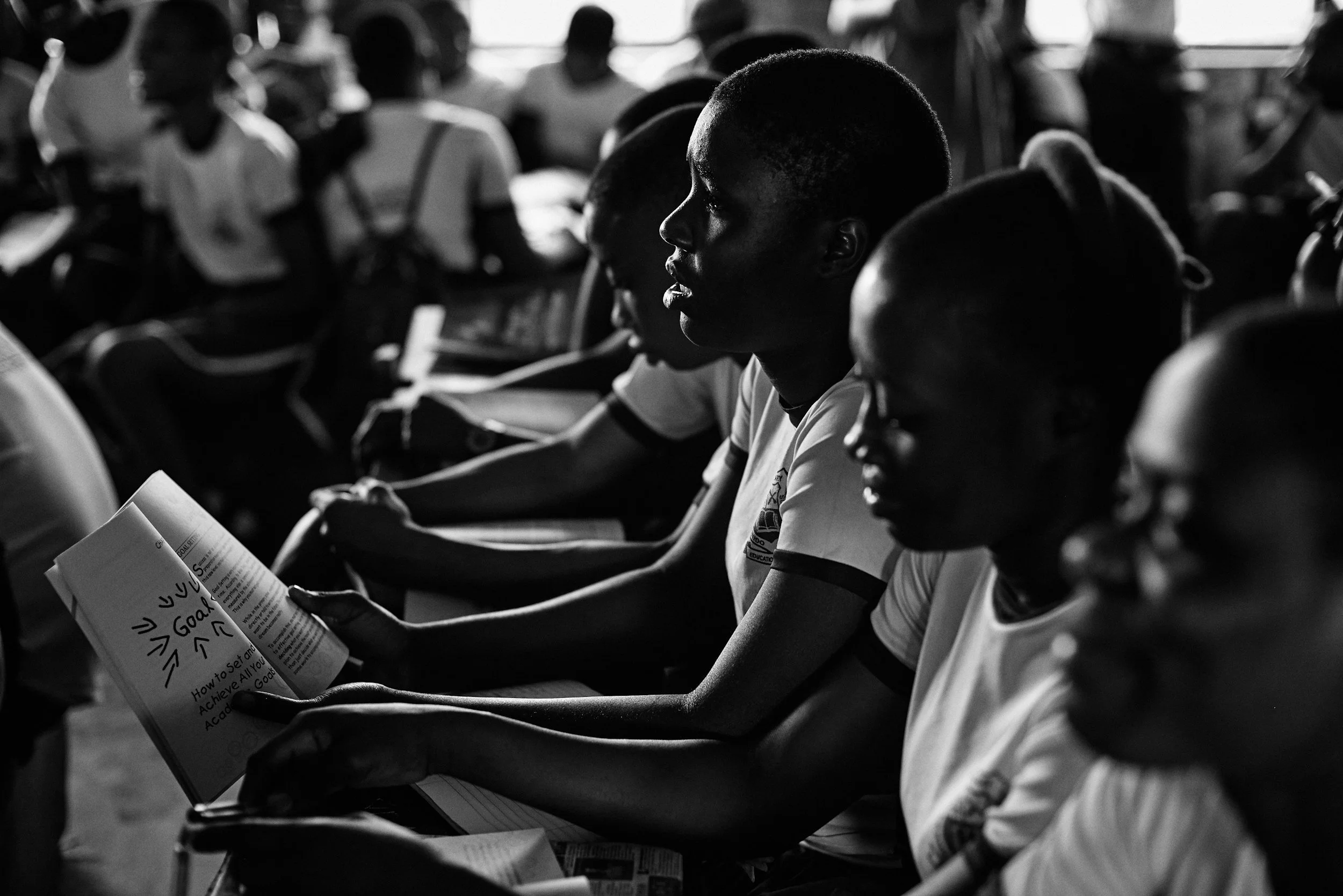A group of students sitting in a classroom, reading a book.