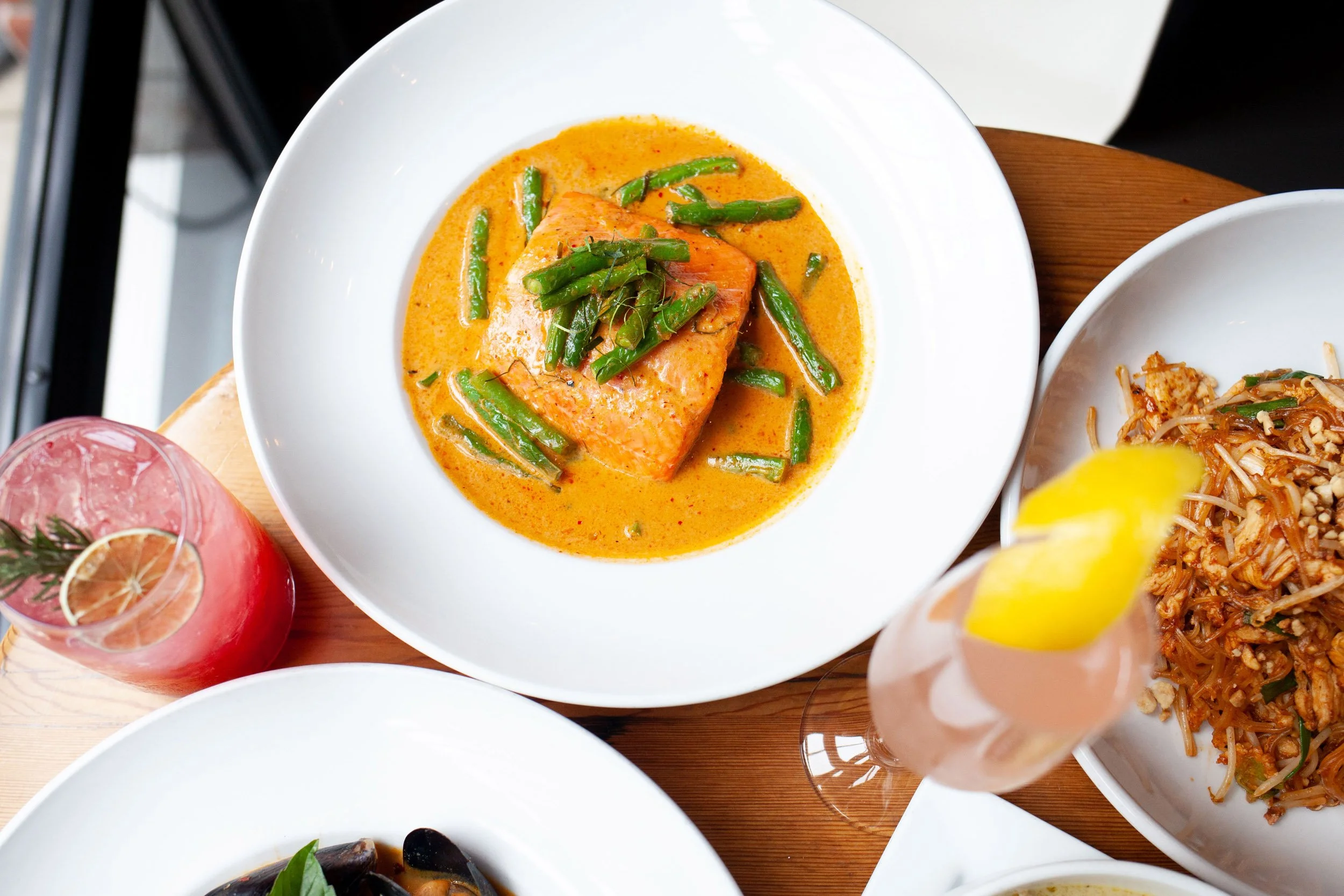 Colorful entree from Sabai’s food menu in Eugene, Oregon featuring salmon curry and green beans with a signature cocktail from the bar.