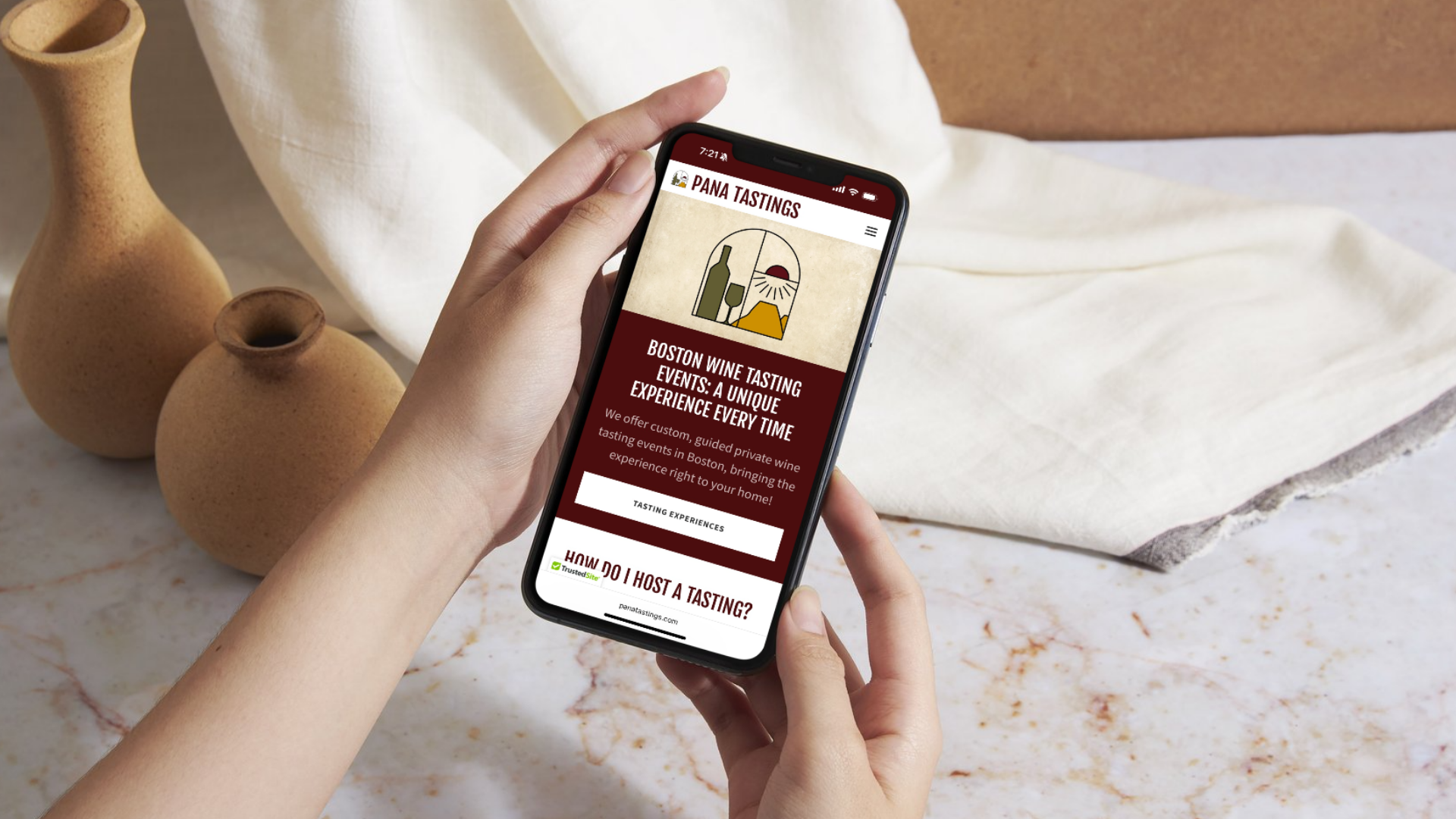 Person holding a smartphone displaying a website for Pana Tastings, which offers guided private wine tasting events in Boston. The phone screen shows a logo with a wine bottle, glass, sun, and mountain, along with text about wine tasting experiences and hosting tips.