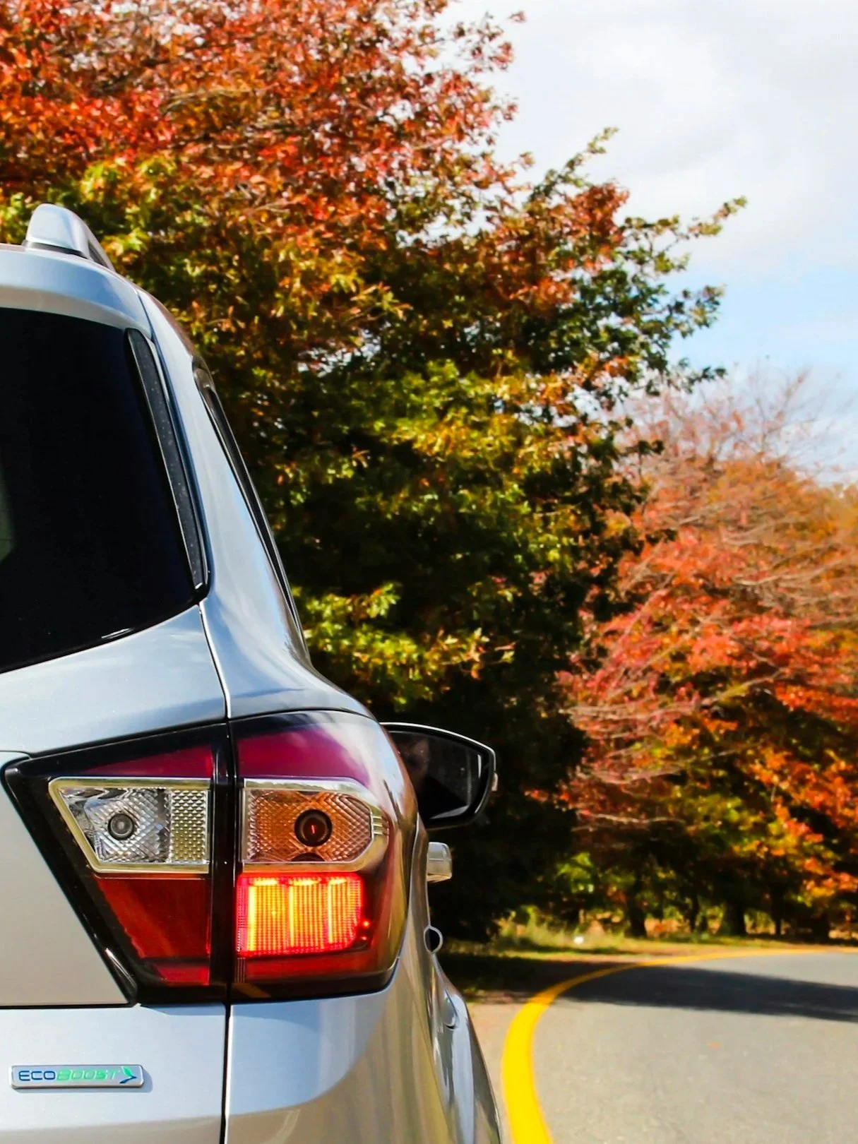 A silver SUV driving on a curved road with autumn trees in the background.