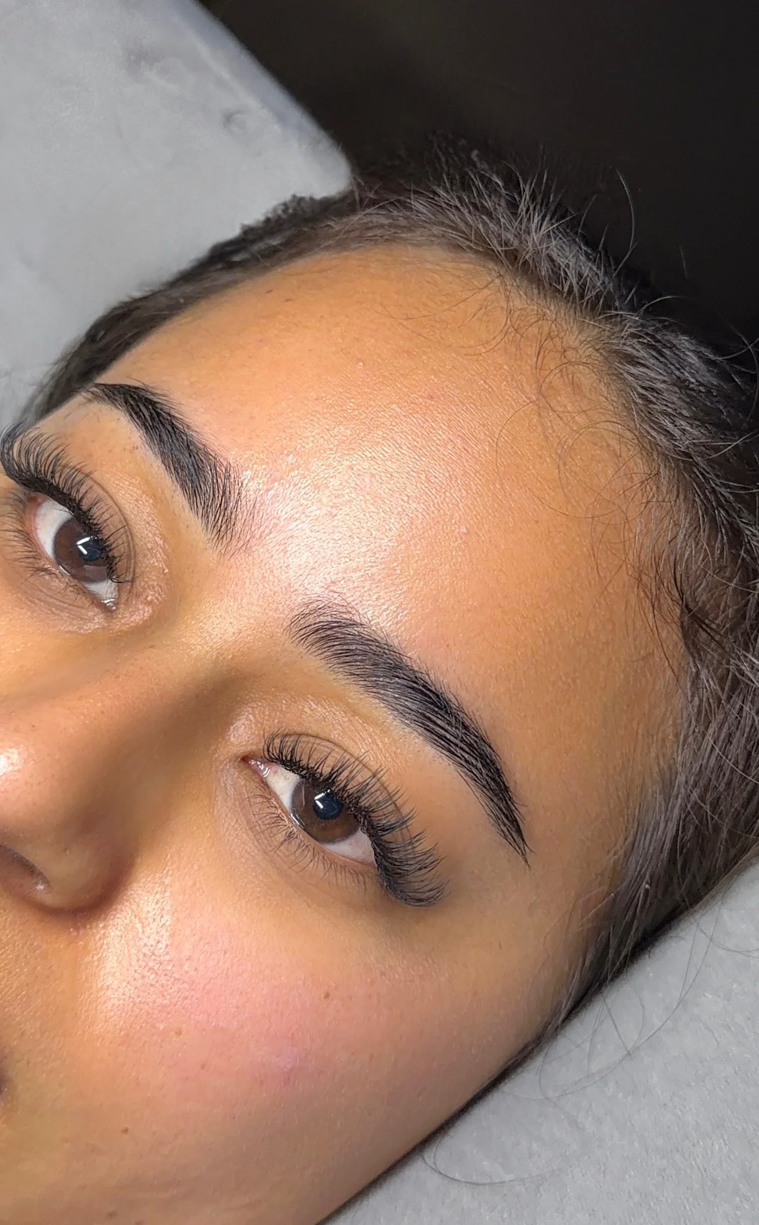 Close-up of a woman's face showing her well-groomed eyebrows and long eyelashes, with smooth skin and natural makeup.