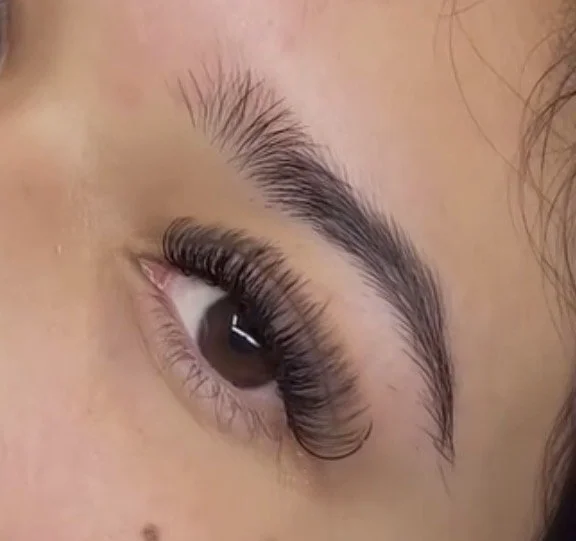 Close-up of a person's eye with long curled eyelashes and well-defined eyebrow.