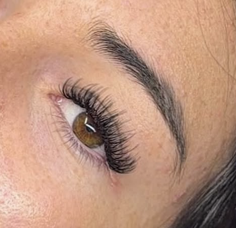 Close-up of a woman's eye with makeup, showing brown eye color, long eyelashes, and well-groomed eyebrows.