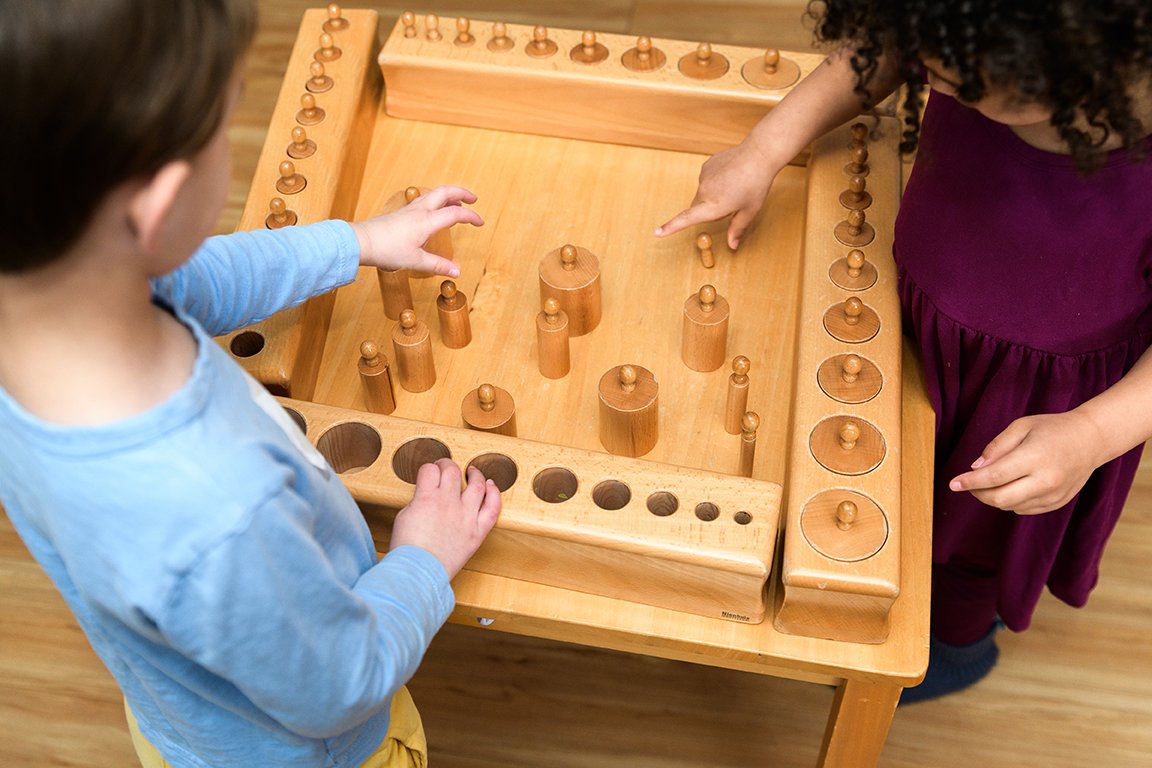 Two children playing a wooden game with pegs on a table.