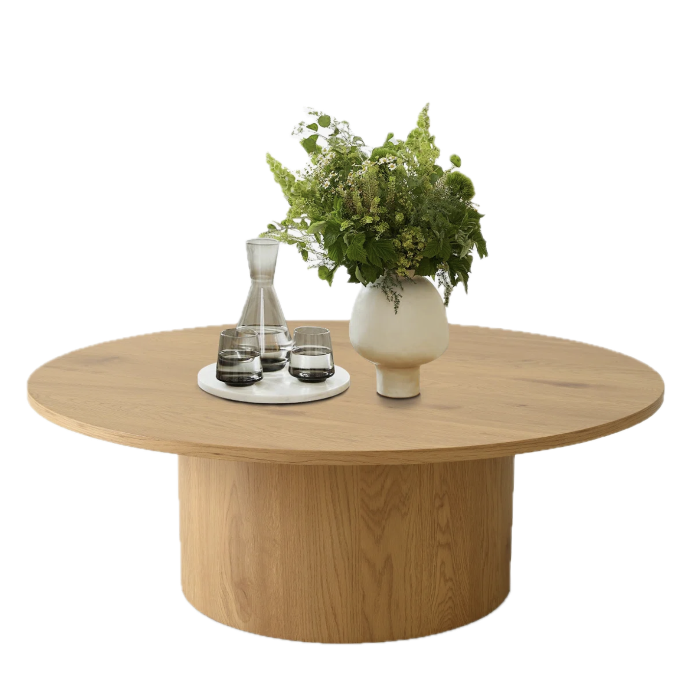 Round wooden table with a white ceramic vase filled with green flowers and a glass carafe with three glasses on a white tray.