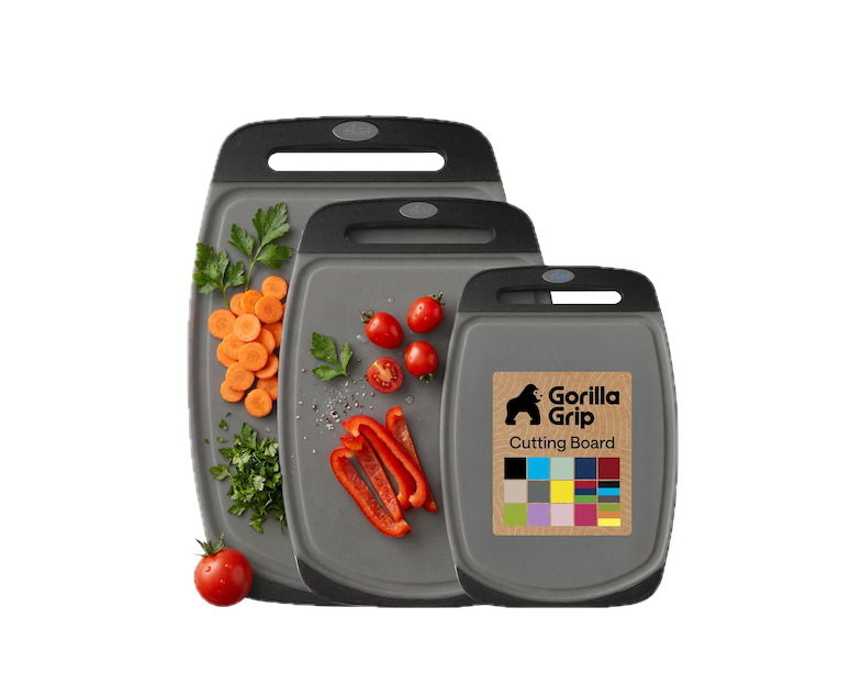 Three Gorilla Grip cutting boards with vegetables arranged on them, including carrots, cherry tomatoes, red bell pepper, and cilantro, with additional vegetables outside the boards and a black background.