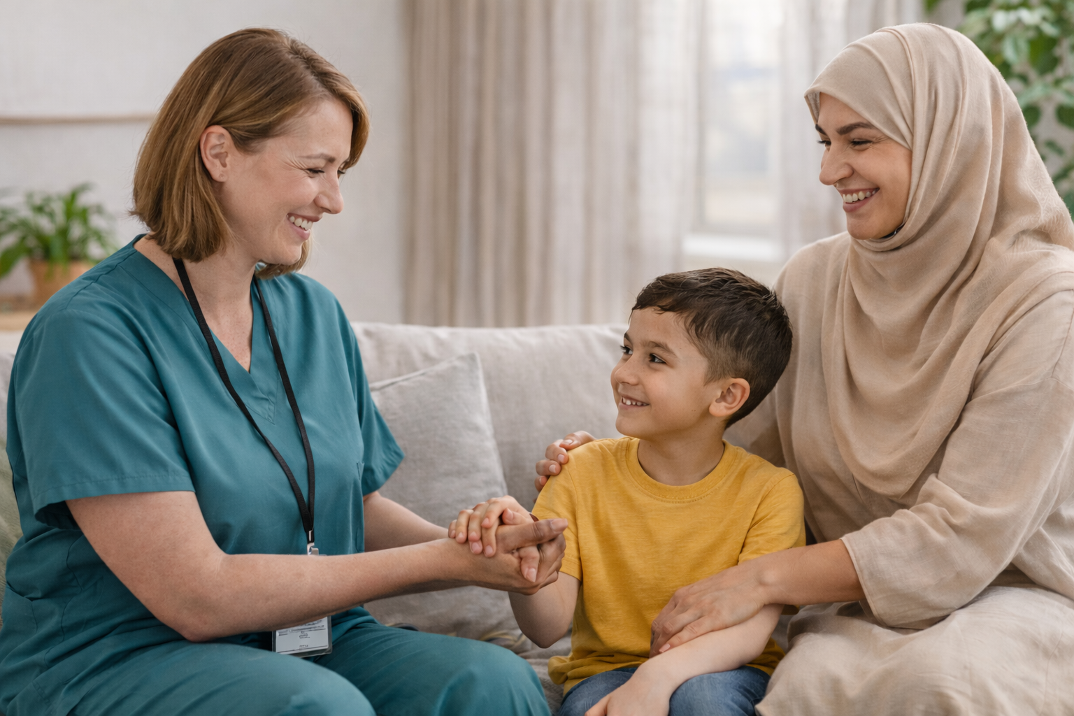 A support worker sitting with a mother wearing a hijab and her young son, smiling and holding the child’s hand during a home visit.